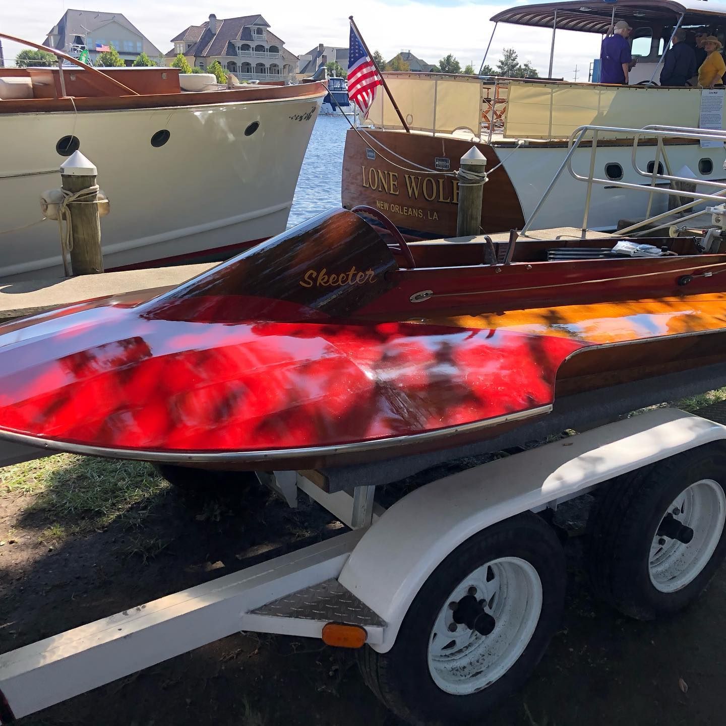 Red and wood speedboat on a trailer at a boat show, with American flag and other boats nearby