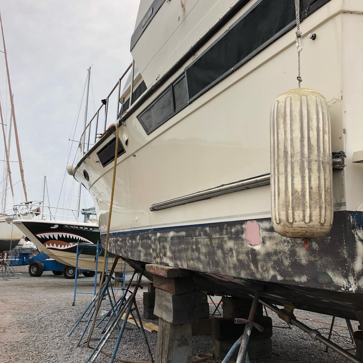 Boat hull on stands in a boatyard, showing weathered black and white paint with a hanging fender.