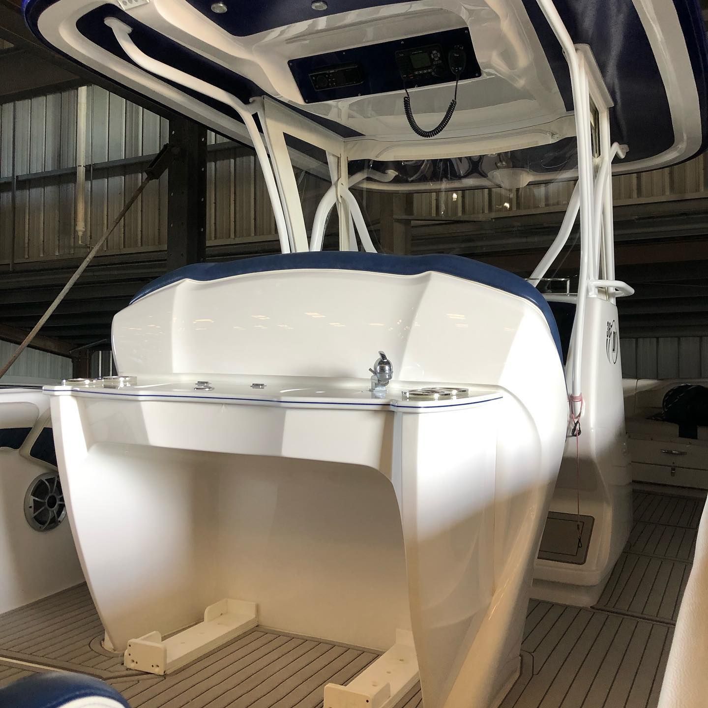 White boat stern under cover in a marina or boatyard, with a canopy frame and tan deck flooring