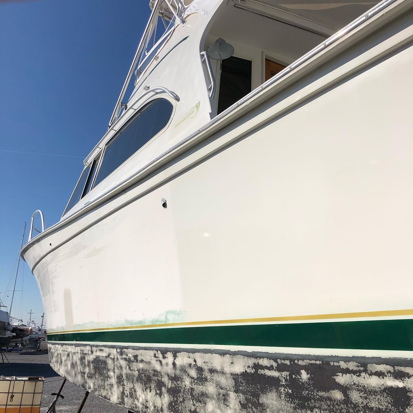 White yacht hull with green stripe at a marina, viewed from below against a blue sky