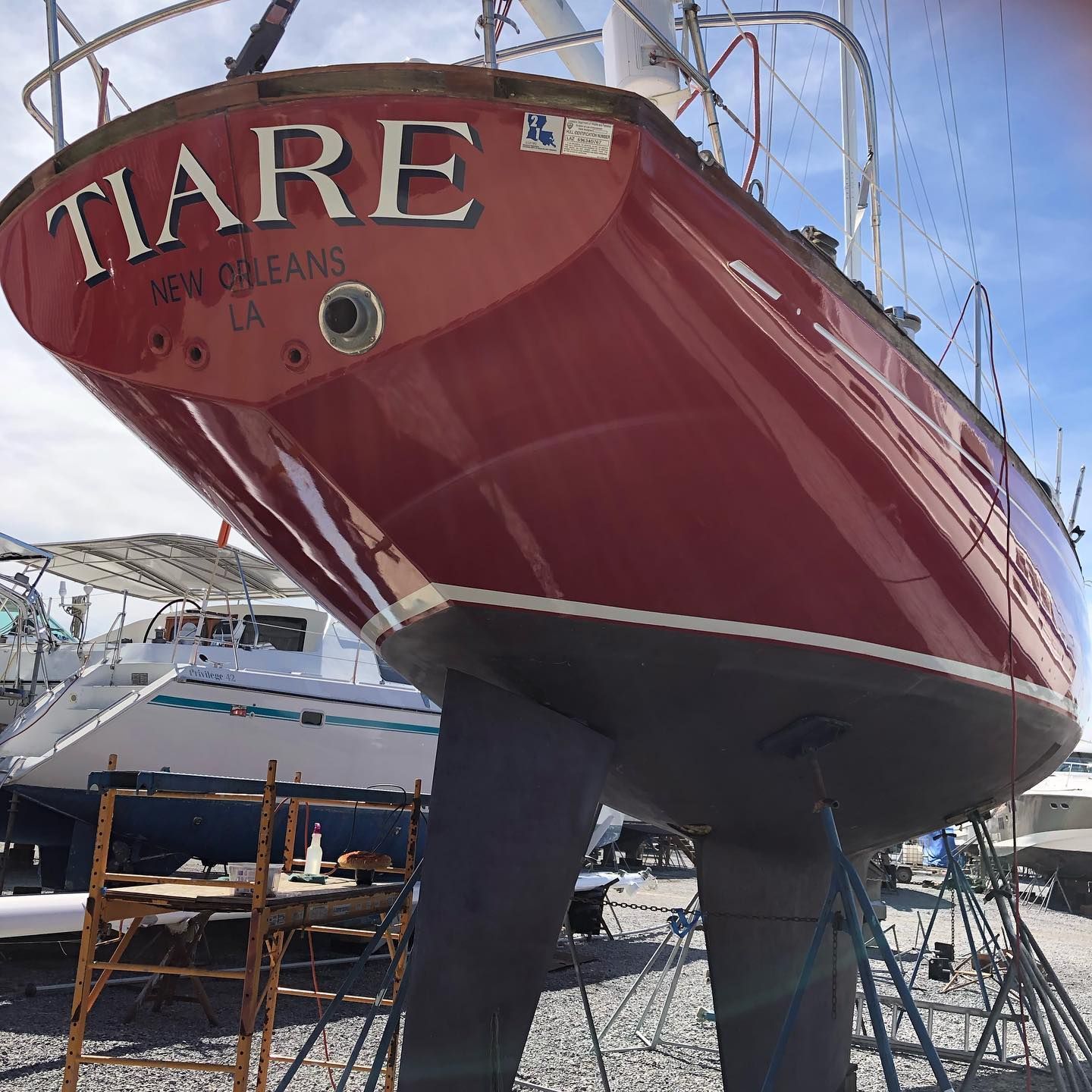 Red sailboat named Tiare on stands in a boatyard, with a red hull and white trim