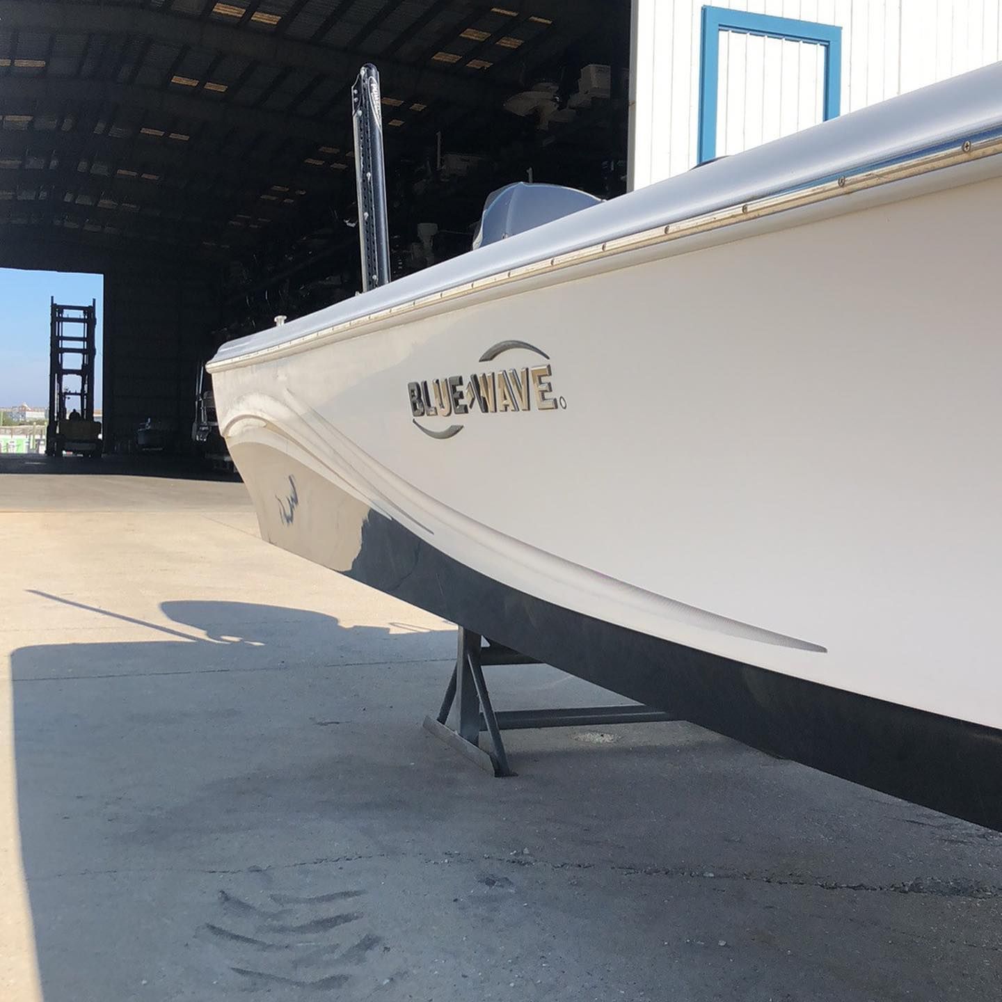 White boat on a trailer outside a boathouse in bright sunlight