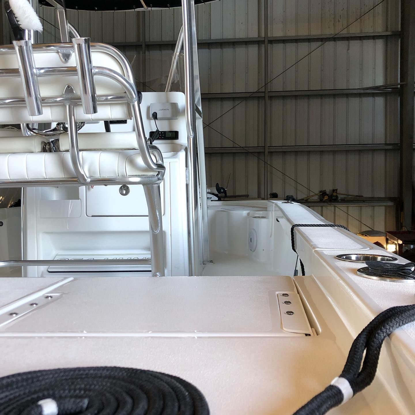 White boat interior with a center console, seating, railings, and coiled black rope in a marina or warehouse.