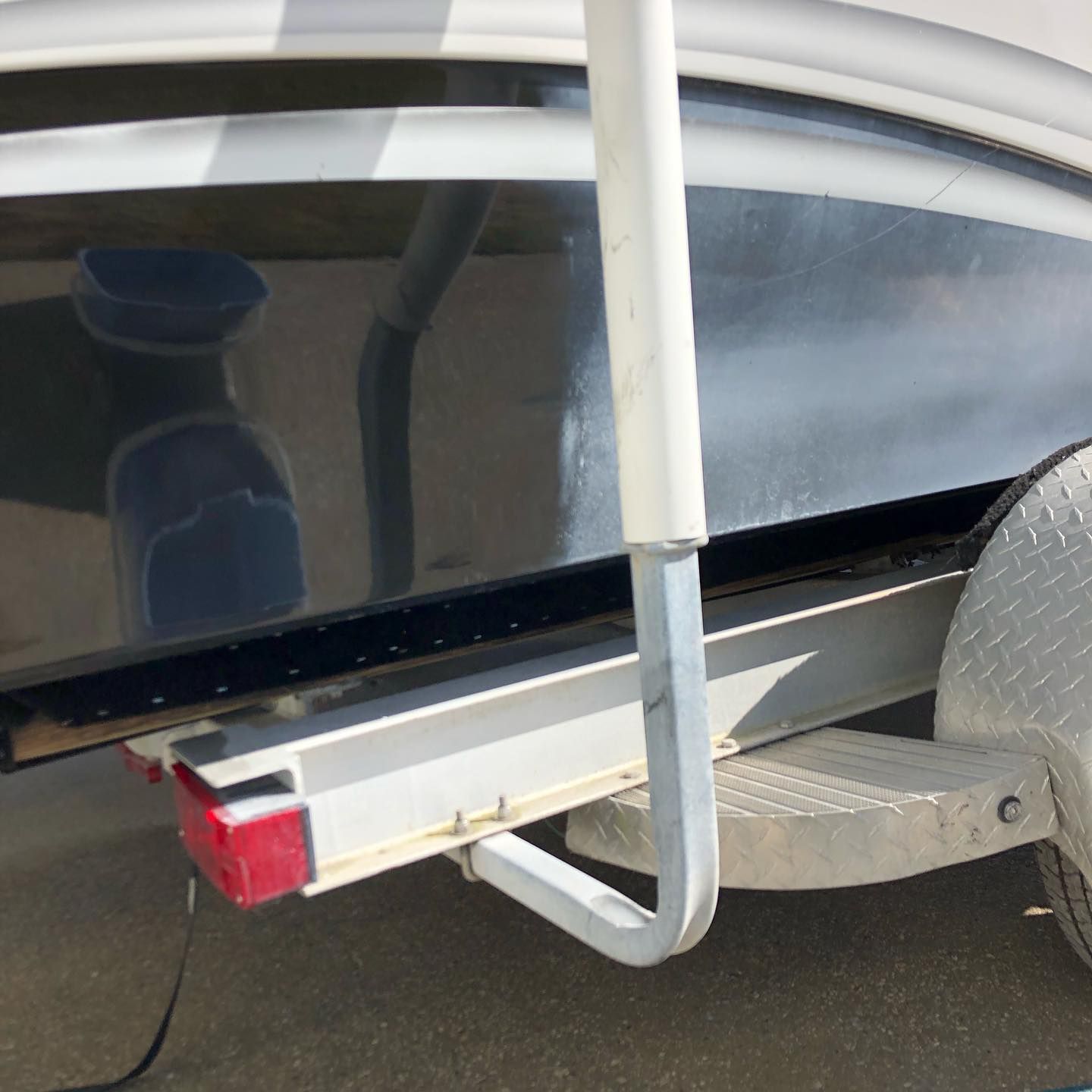 Close-up of a boat trailer hitch and rear step with a red reflector, next to a gray patterned seat.