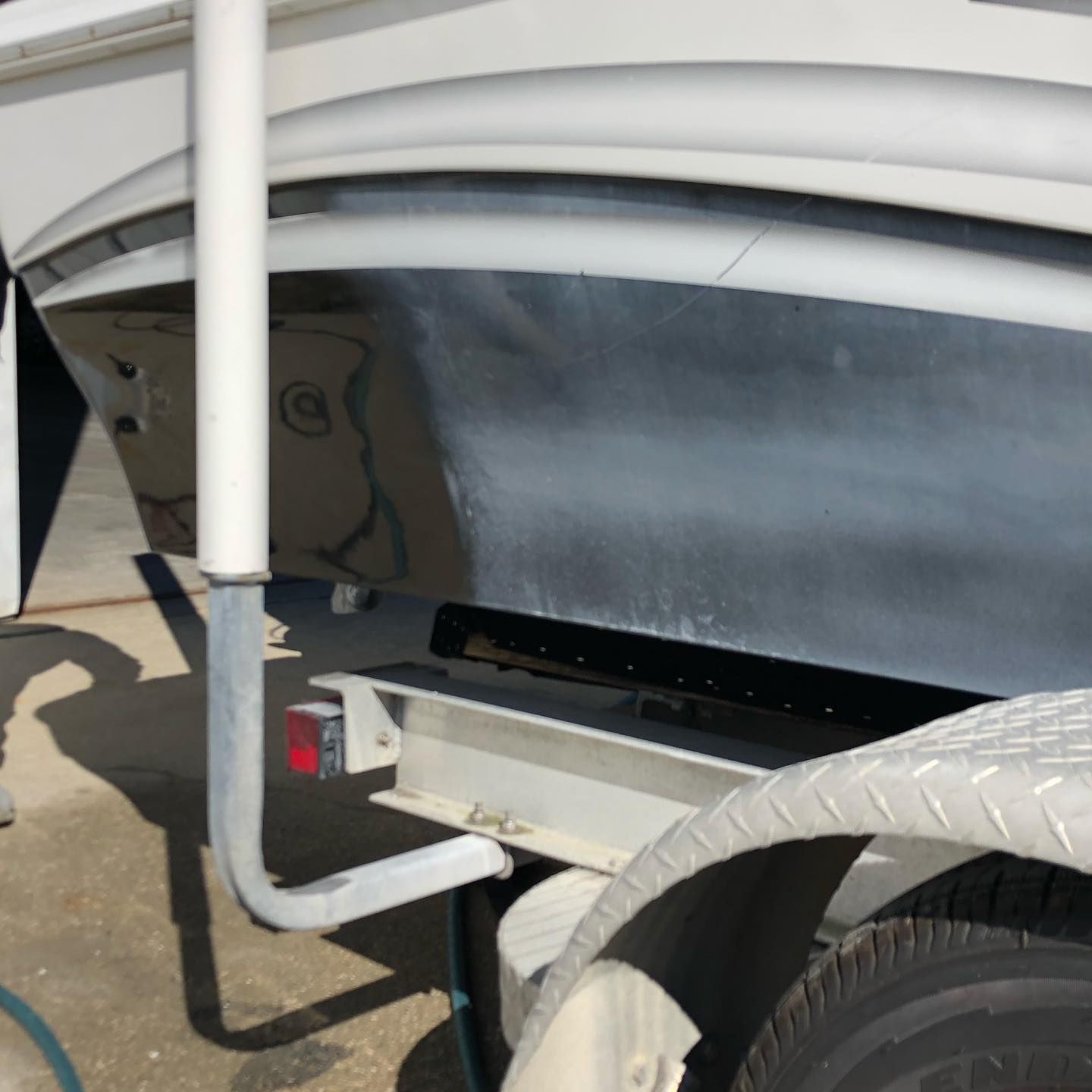 Close-up of a white trailer hitch and wheel with a gray lower panel and braided hose.