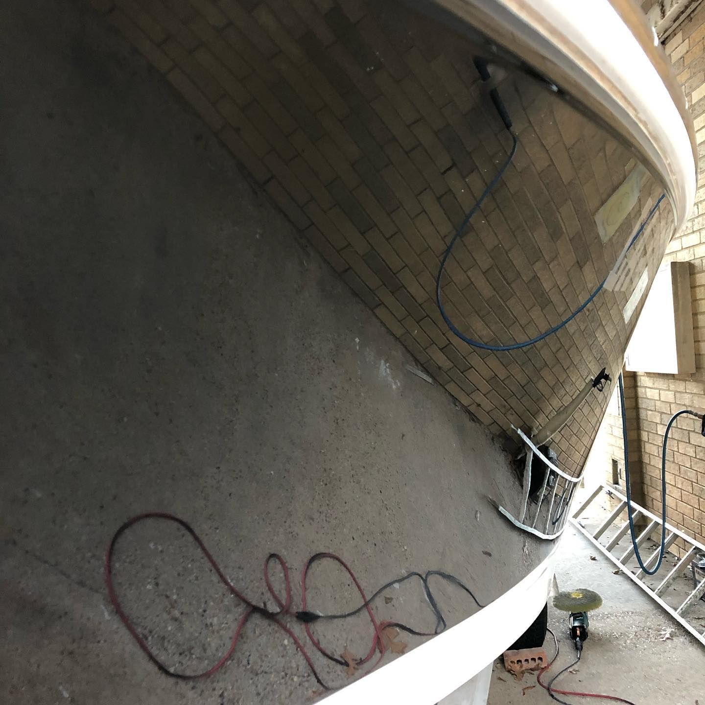 Cylindrical concrete wall with hanging wires and a person working near the bottom in a narrow outdoor space