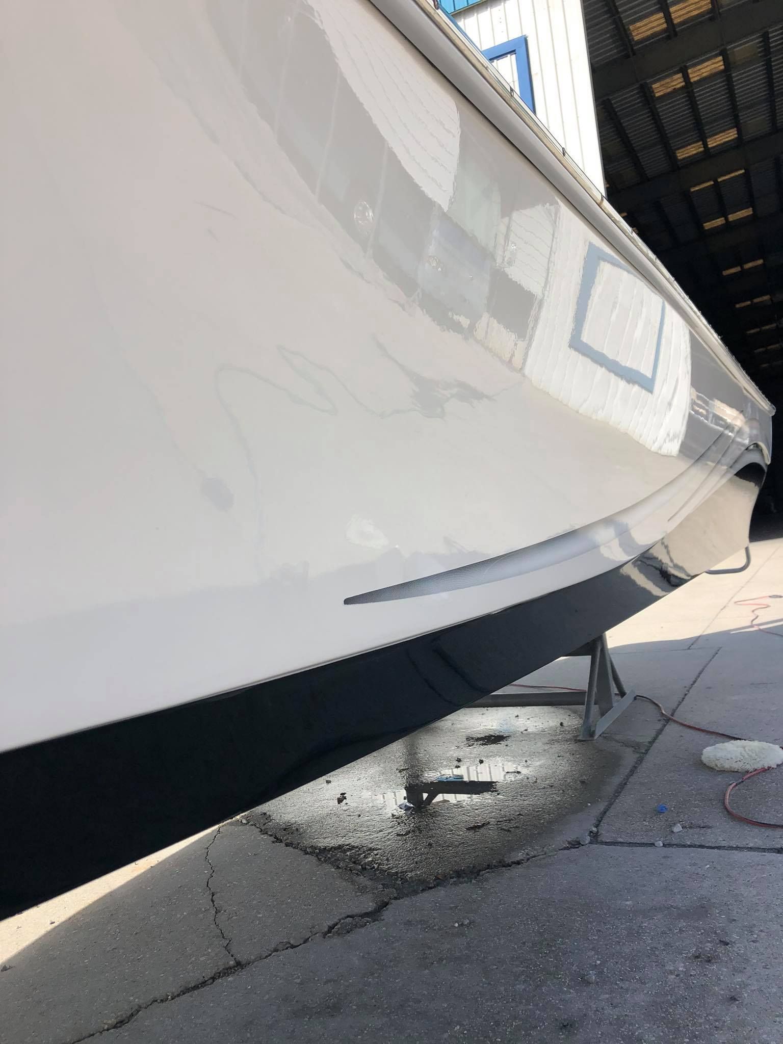 Close-up of a white boat hull over a wet dock, with water dripping onto the pavement.