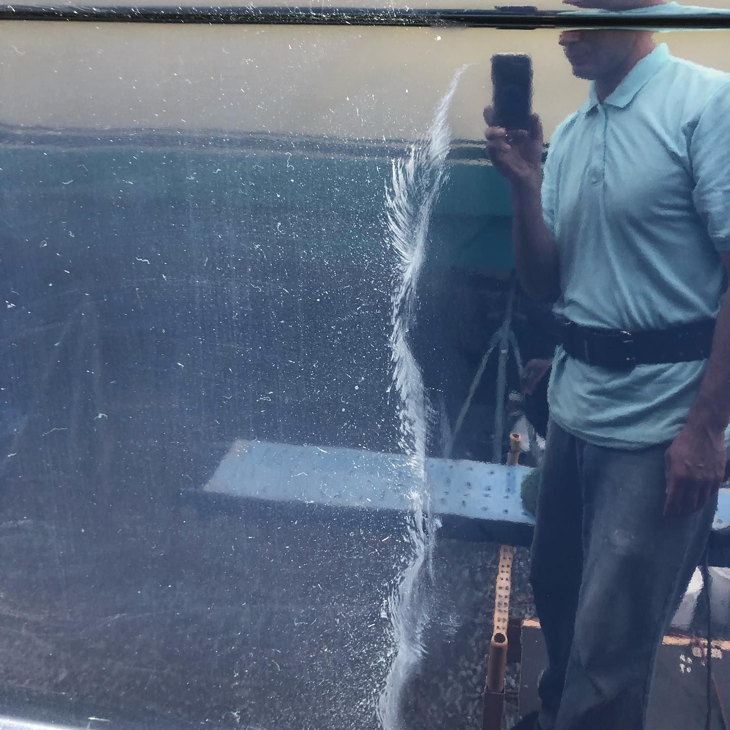 Person in a light blue shirt holding a phone beside a large window with water splashing down it.