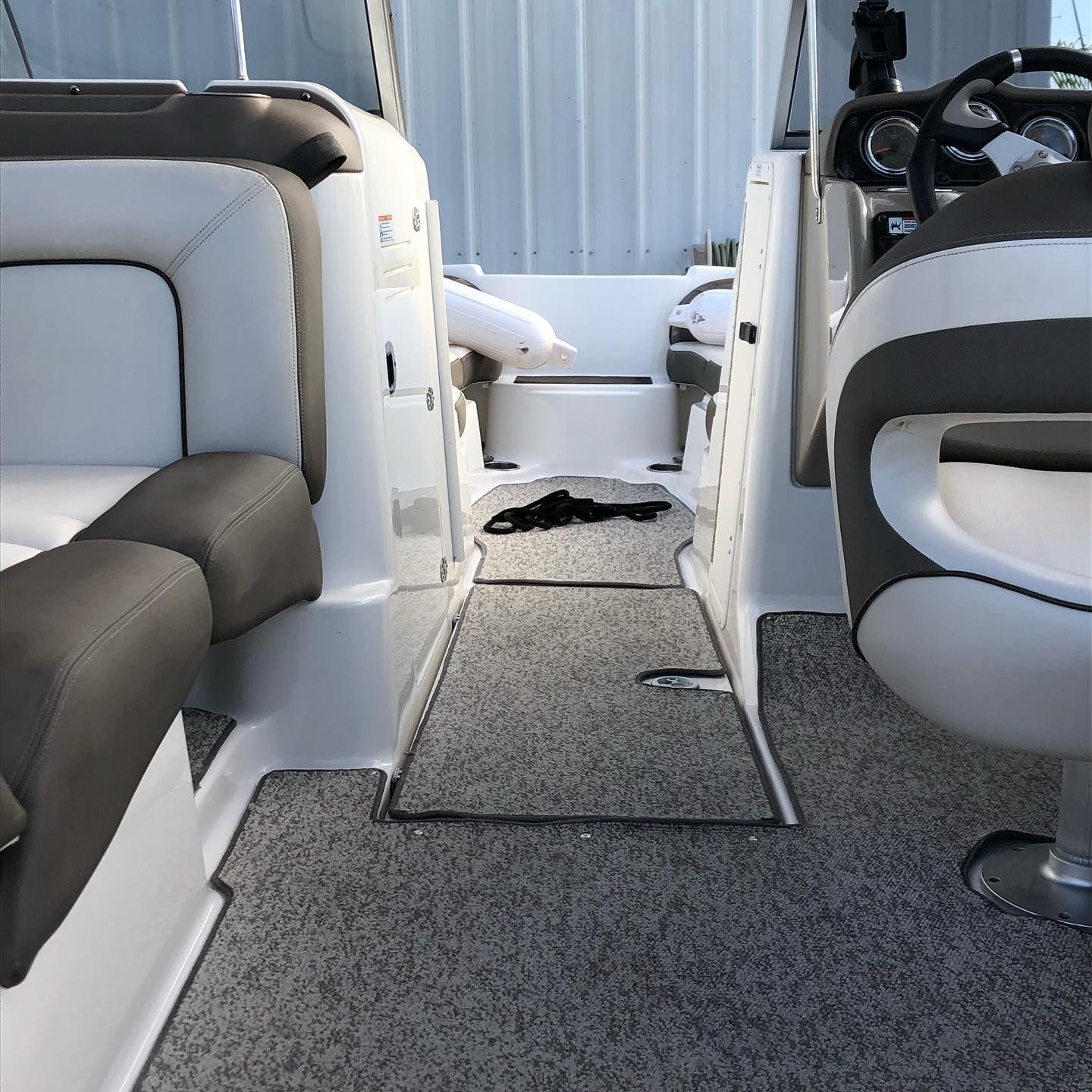 Boat cabin aisle with gray carpet between white-and-gray seats and a black mat on the floor
