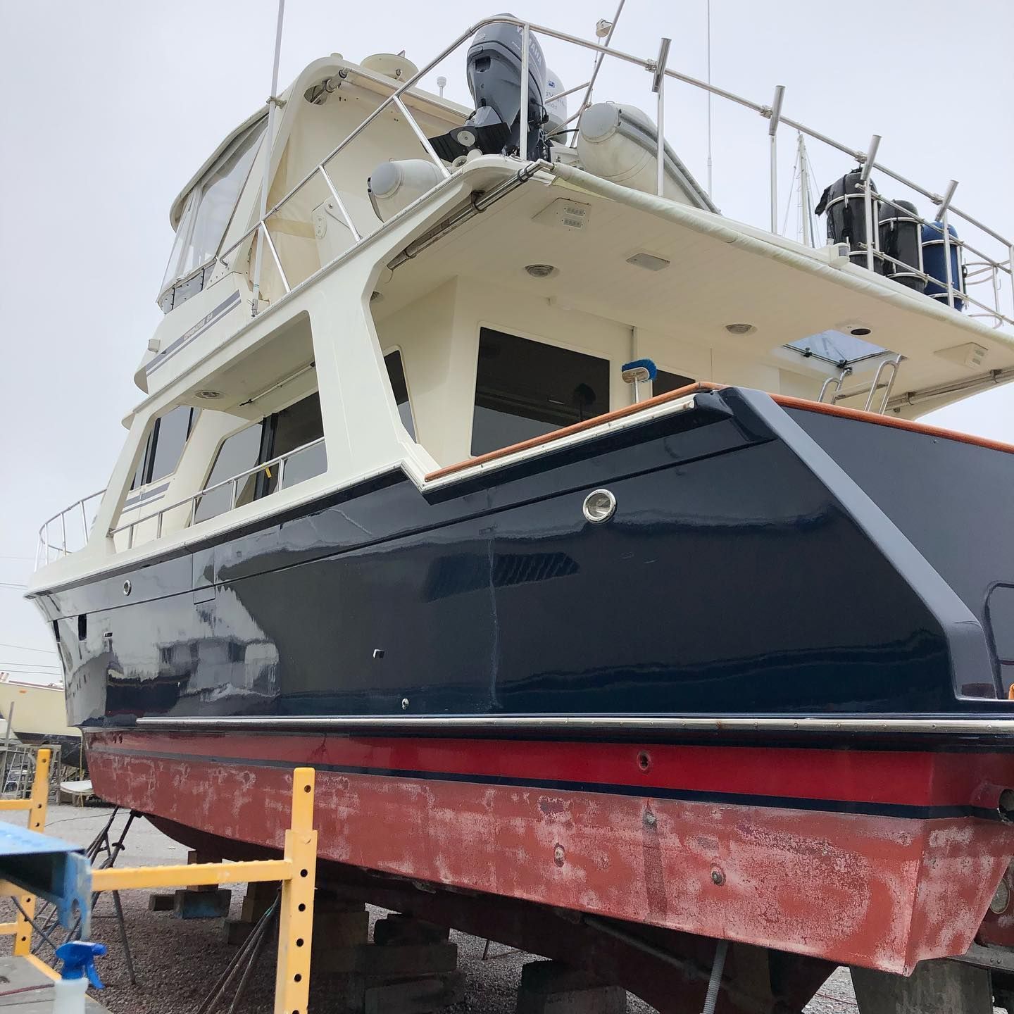 Large white and navy yacht on supports in a boatyard, viewed from the bow.