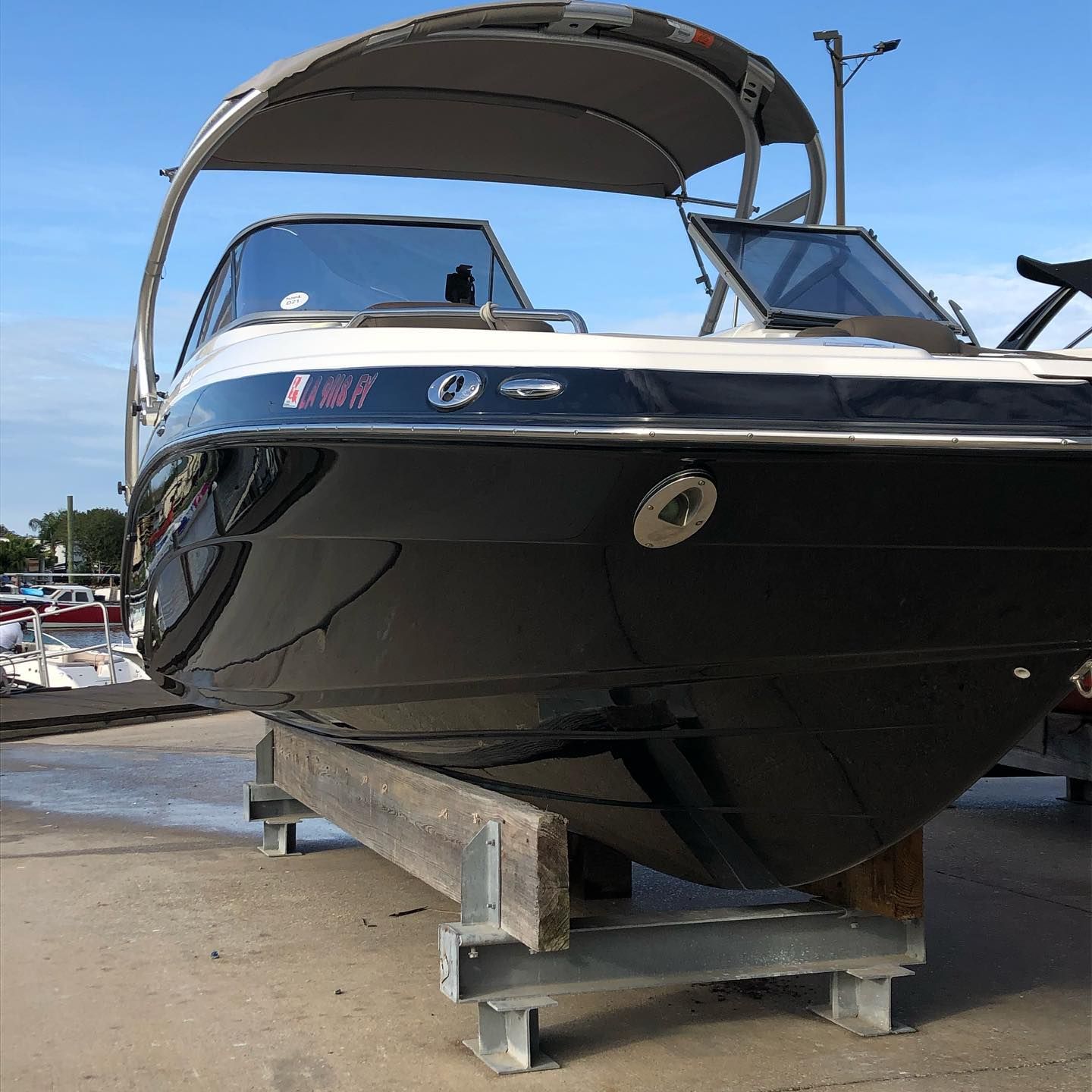 Black speedboat on a trailer at a marina, viewed from the front under a canopy.