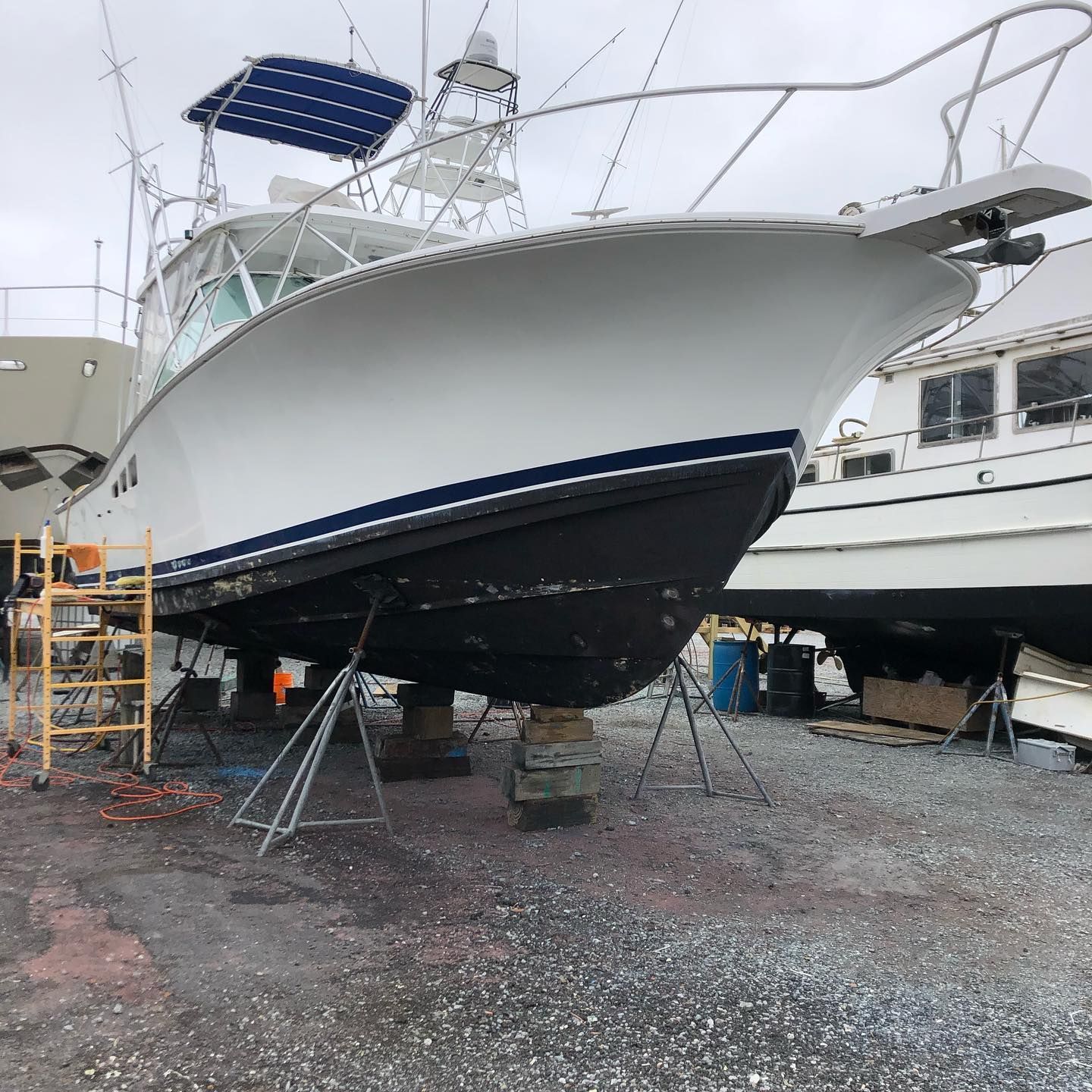 Large white boat on stands in a gravel boatyard, with a blue solar panel on top.