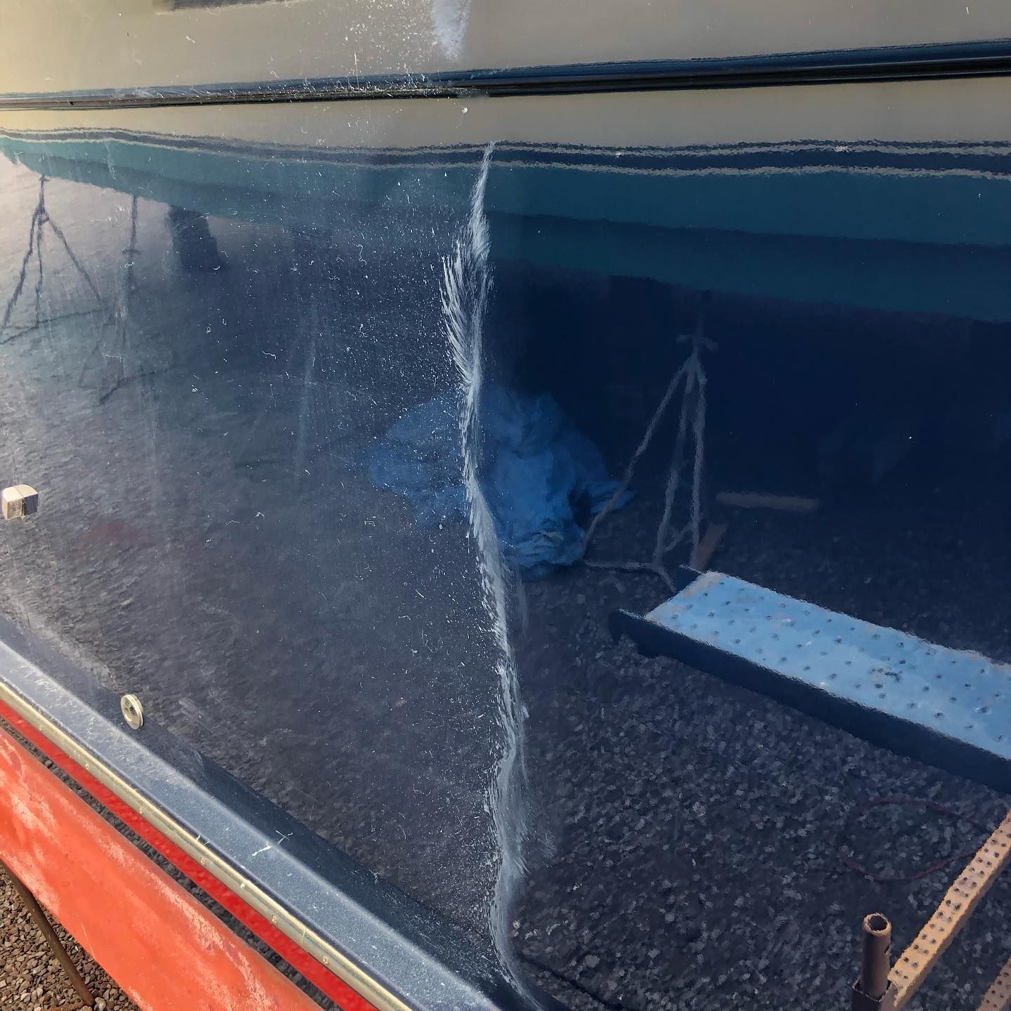 Close-up of a scratched blue boat hull with a red stripe and reflections on glossy paint.