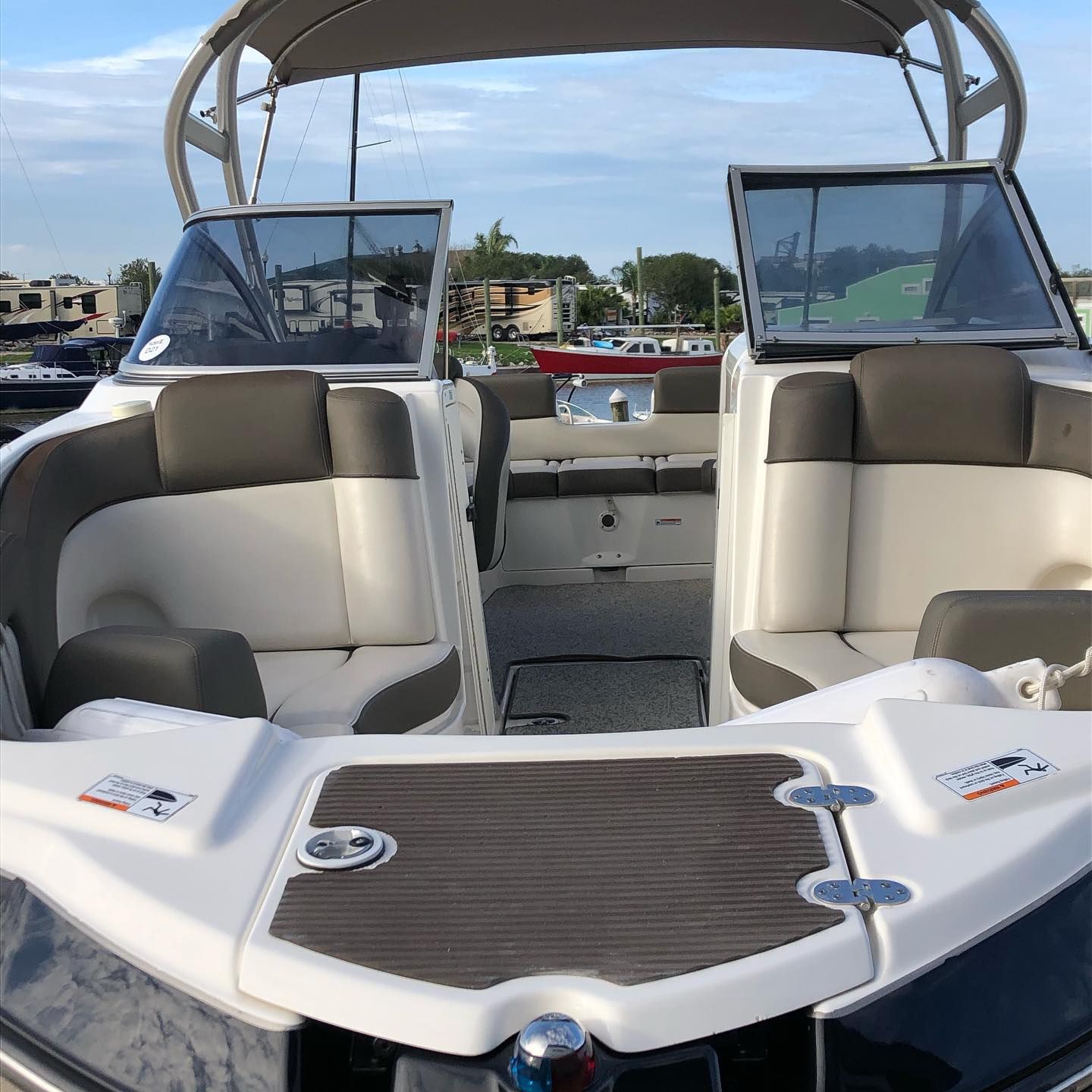 Boat cockpit with two white-and-gray captain’s chairs, open windshield, and a canopy overhead.