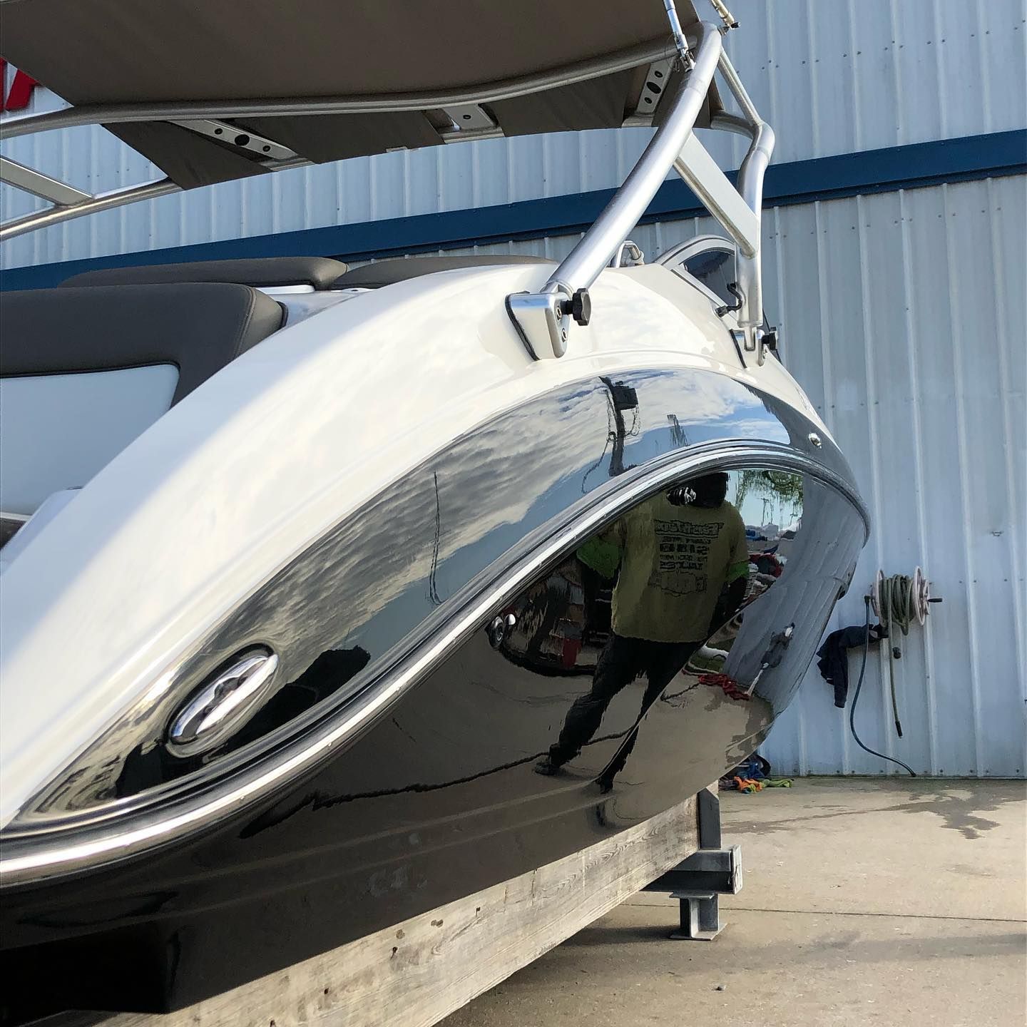 White and black boat on a trailer inside a covered storage area, with a chrome hull reflecting the surroundings