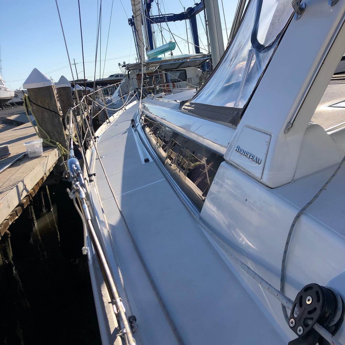 White sailboat deck and cabin along a dock, with rigging and bright blue sky in the background