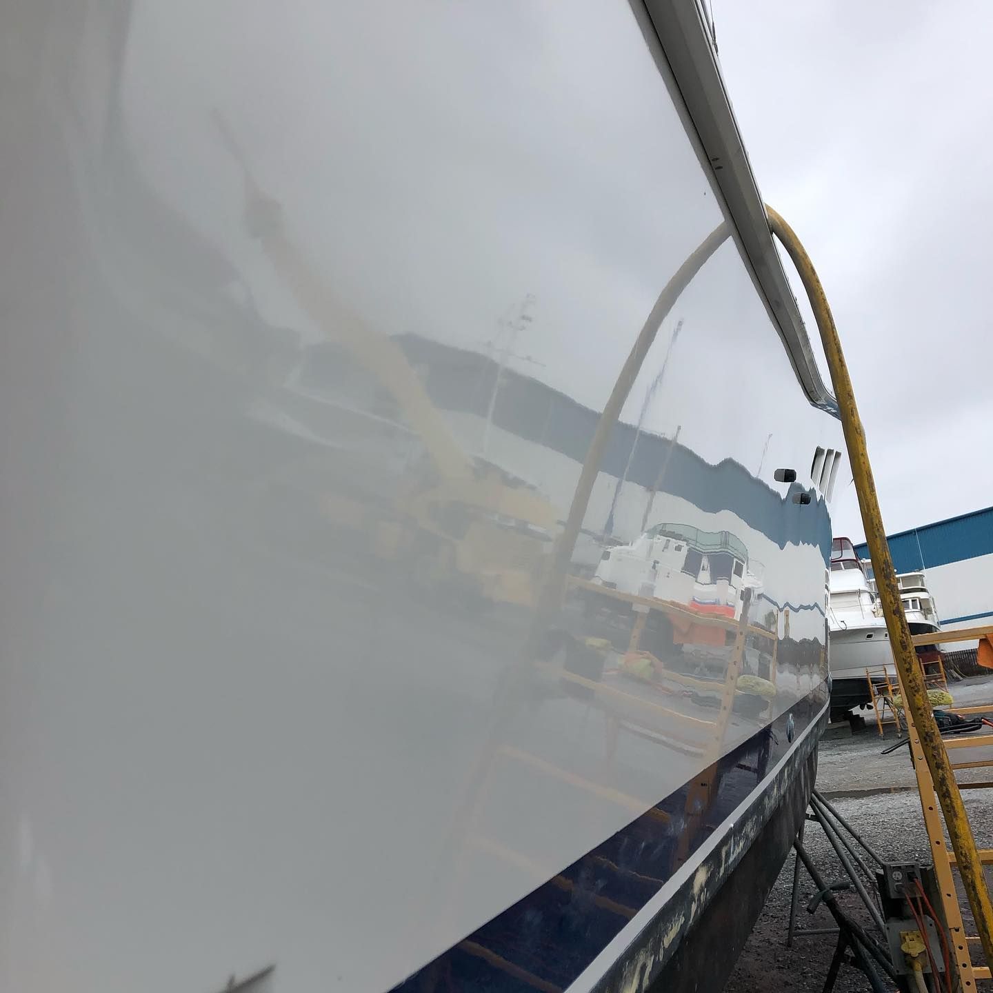 Close-up of a white boat hull reflected at a dock with yellow rope and marina equipment in view