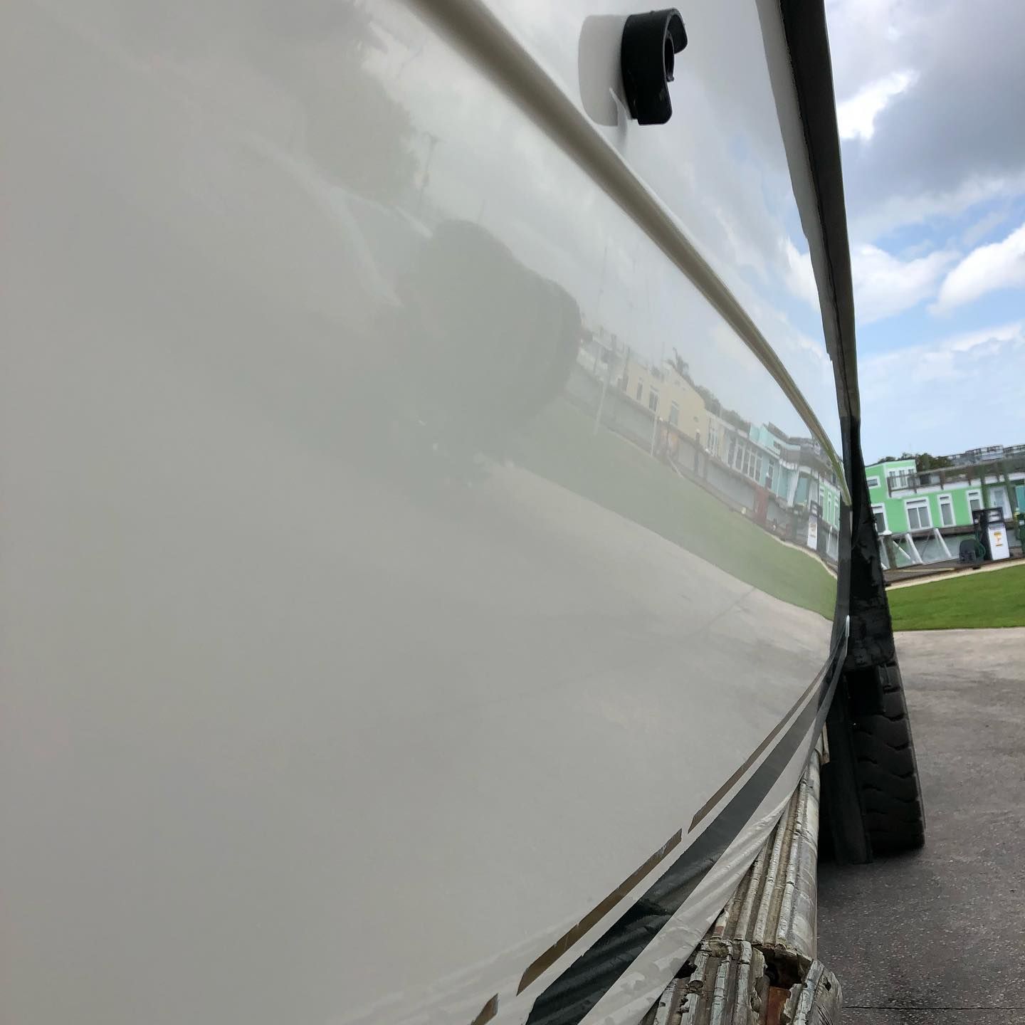 Side view of a white boat hull and black tire fender at a dock, with buildings reflected in the glossy surface.