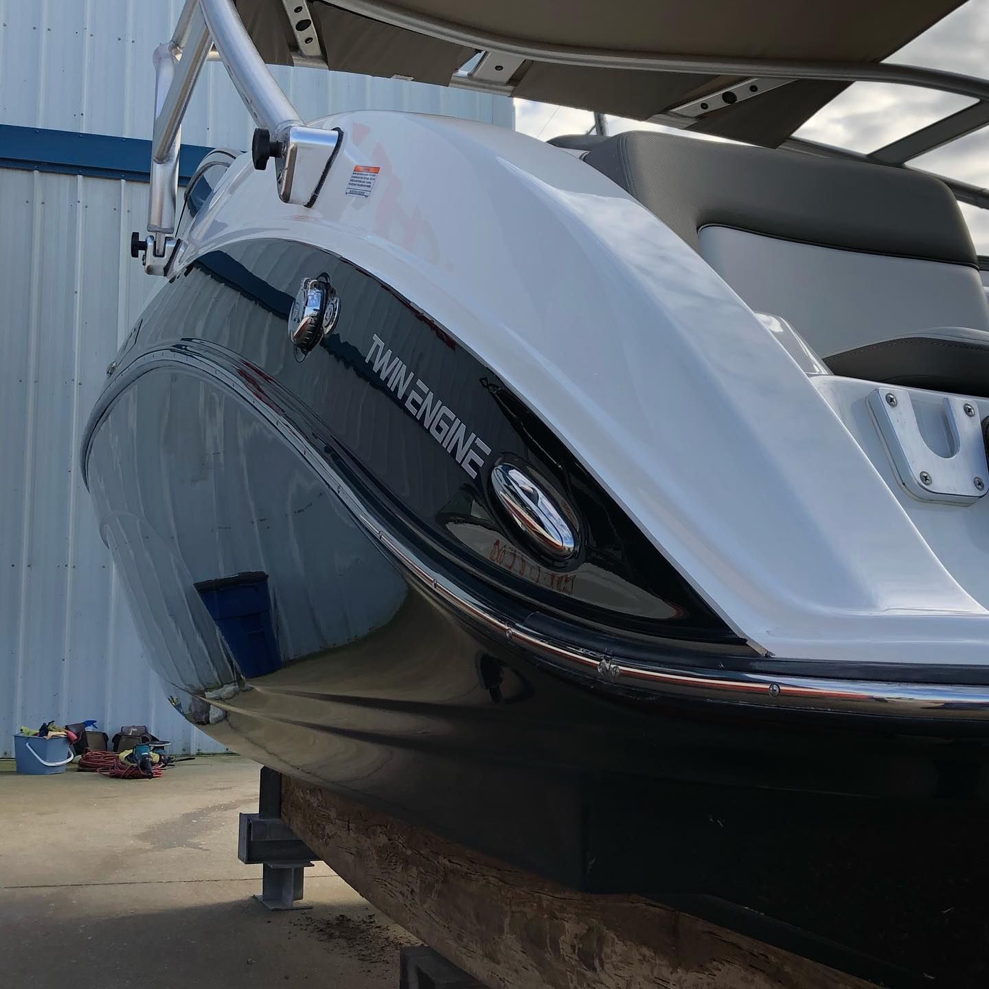 White and black boat hull on a trailer beside a metal building, with water visible inside the cockpit.