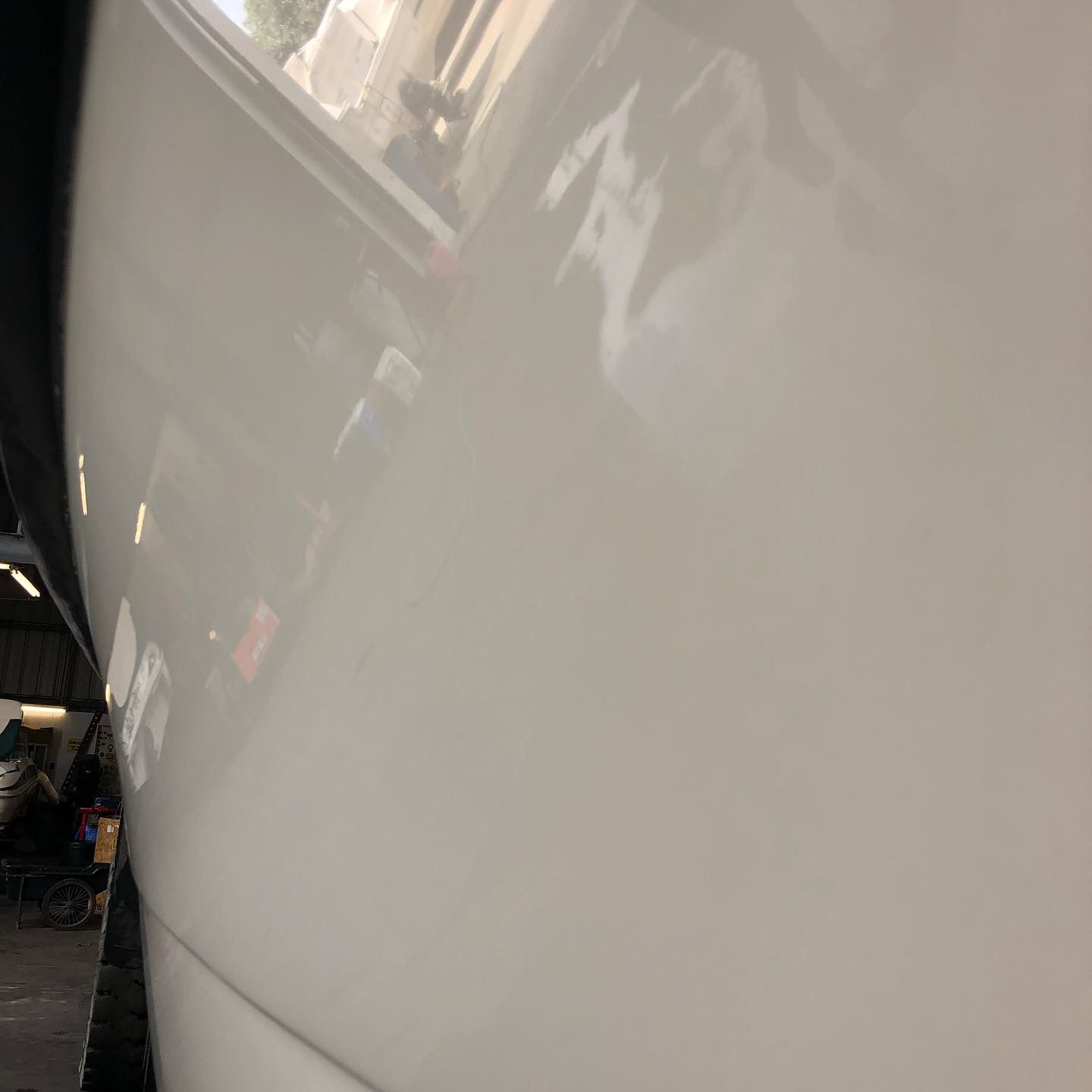 Close-up of a white car’s glossy side panel with reflections in a garage.