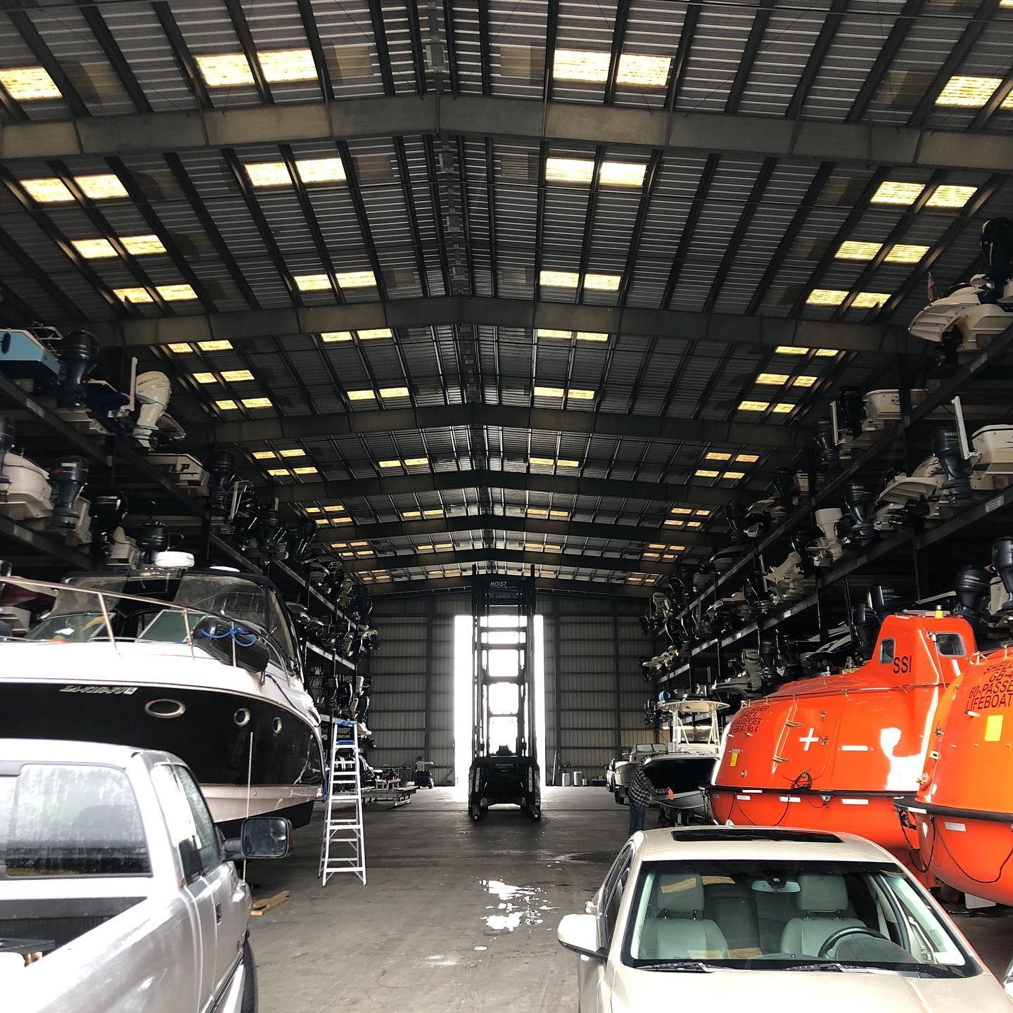 Boathouse interior with several boats, including a bright orange rescue boat and a large black yacht.