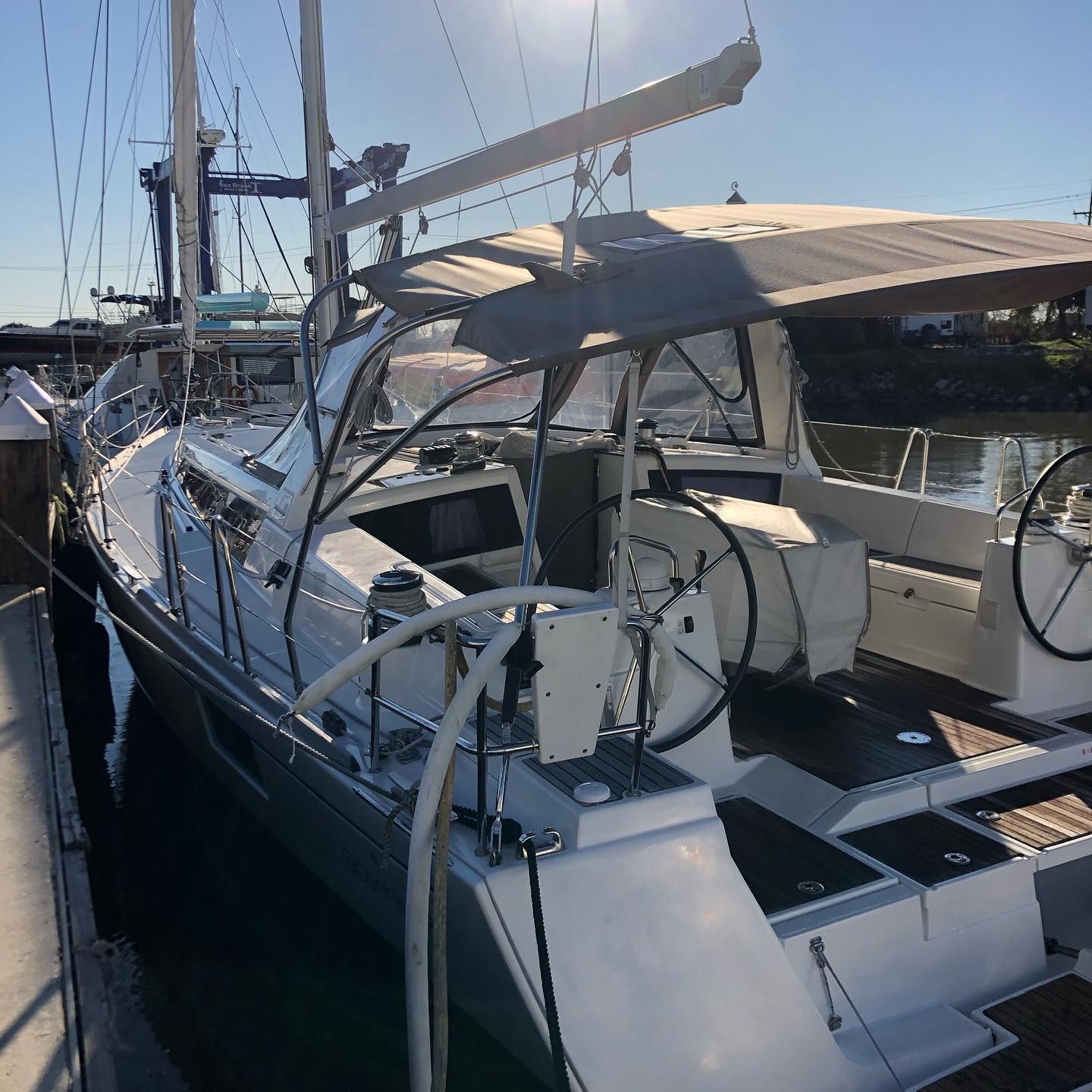 Sailboat docked at a marina, with canopy, rigging, and calm water beside the pier