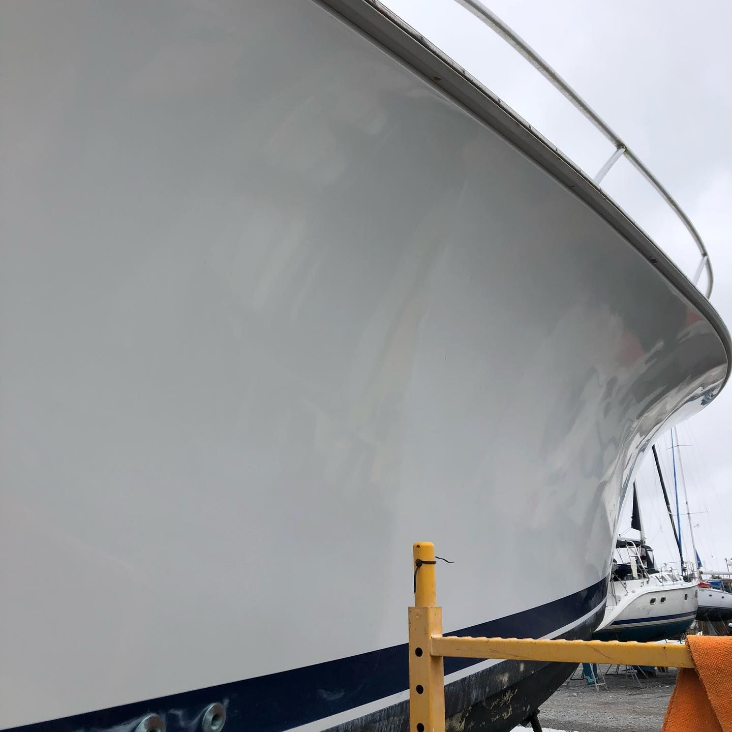 Close-up of a large white boat hull docked beside yellow mooring posts in a marina