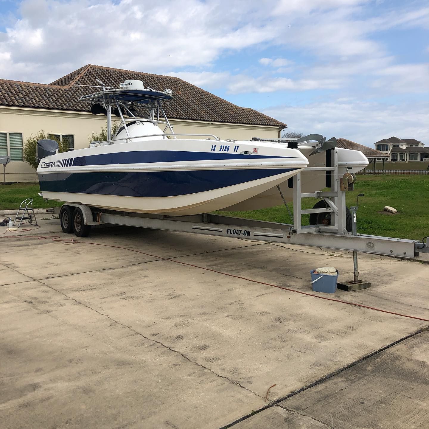 White-and-blue speedboat on a trailer in a driveway beside a house under a cloudy sky