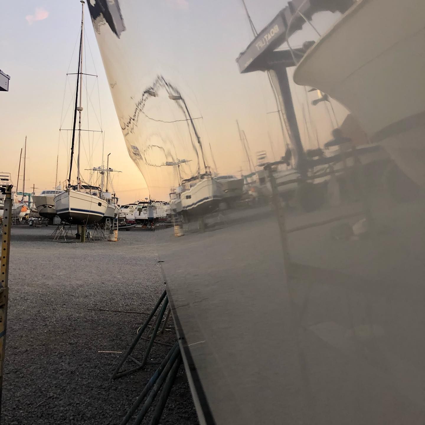Sailboats and masts at a marina at sunset, reflected in a boat hull.