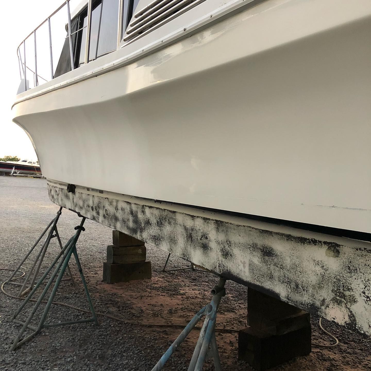 Boat hull in dry dock, supported on stands, with stained lower side over gravel ground.