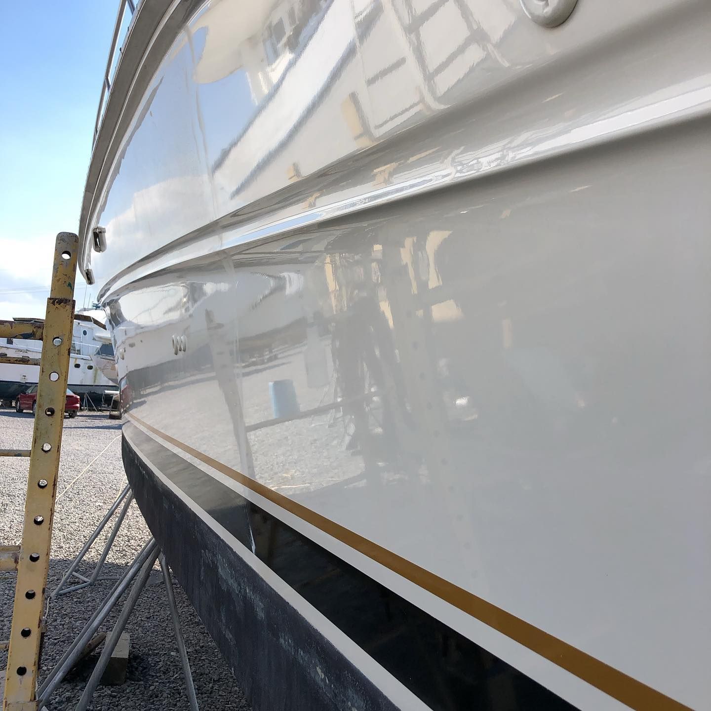 Close-up of a white boat hull with gold and black trim, standing on a boatyard support.