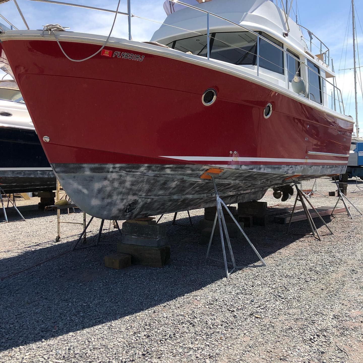 Red-and-white boat on stands in a gravel boatyard under bright sunlight.