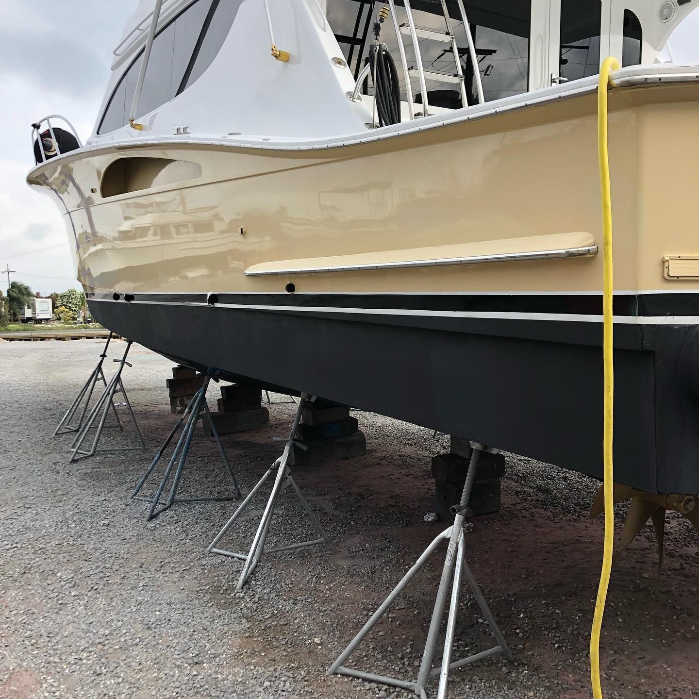 Large cream-and-black boat on metal supports in a boatyard, with a yellow strap hanging beside it.