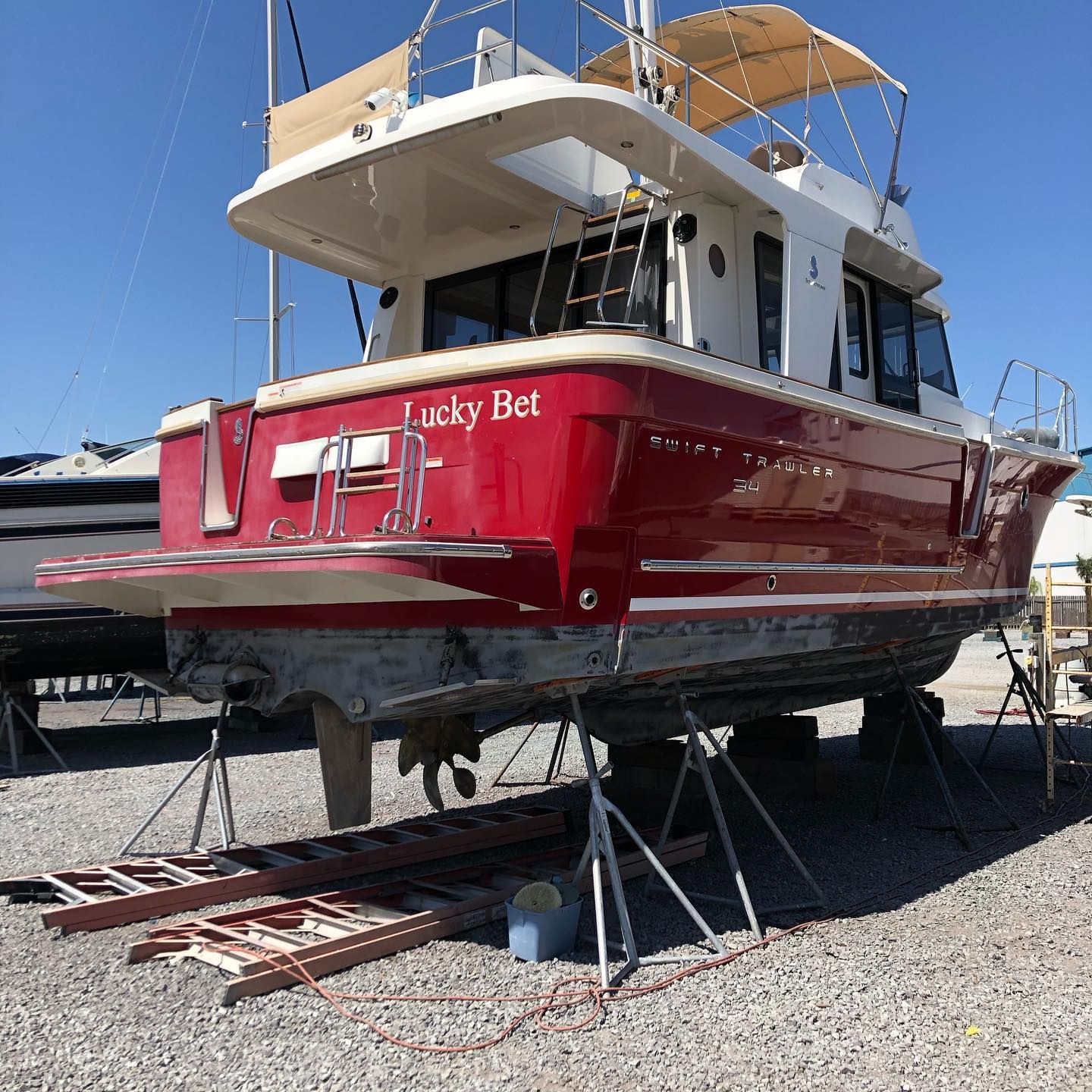 Red and white boat on a cradle in a boatyard under a blue sky