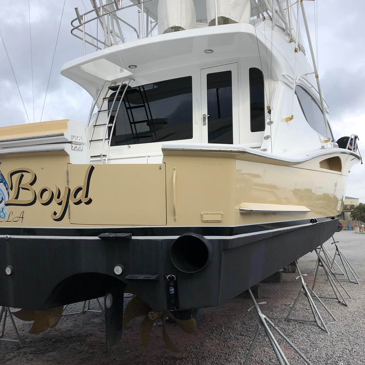White and tan fishing boat named Boyd on a trailer in a boat yard
