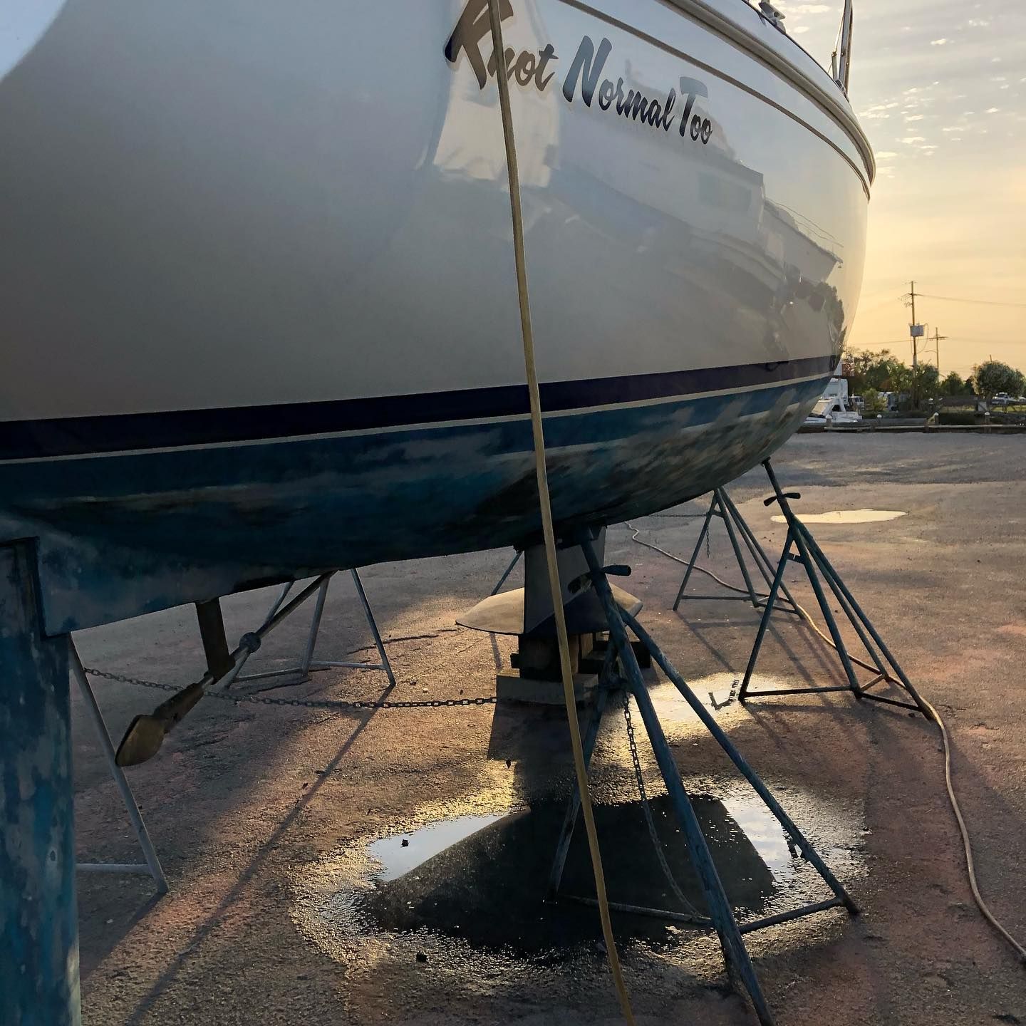 Boat on stands in a boatyard at sunset, with wet pavement and a blue hull.