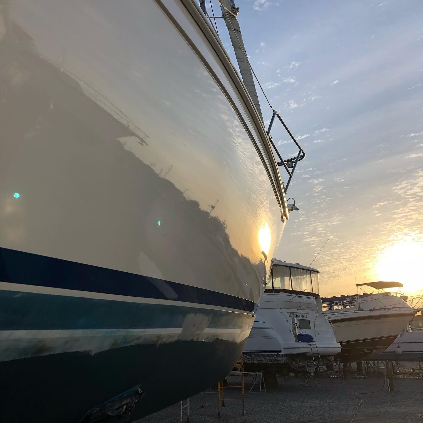 Large white boat in a marina at sunset, with other yachts and warm reflections on the hull.