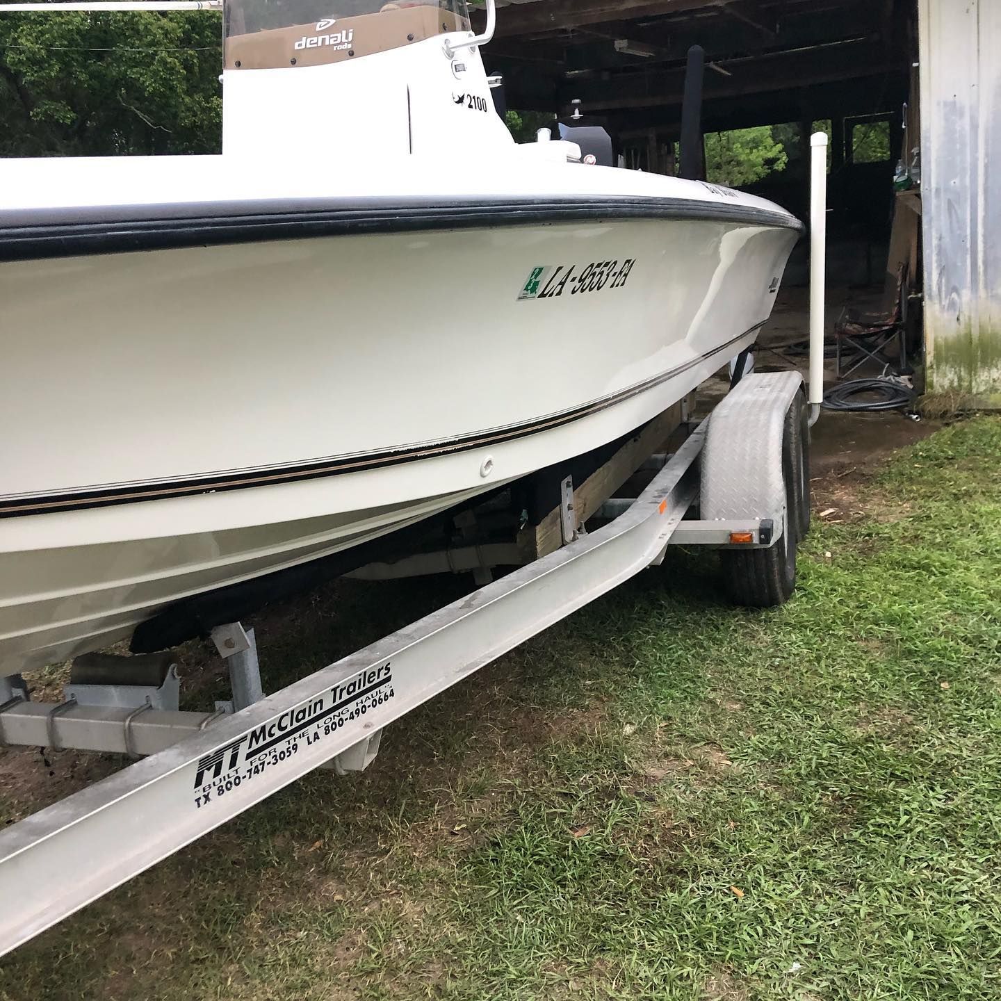 White speedboat on a trailer in a grassy driveway near a garage.