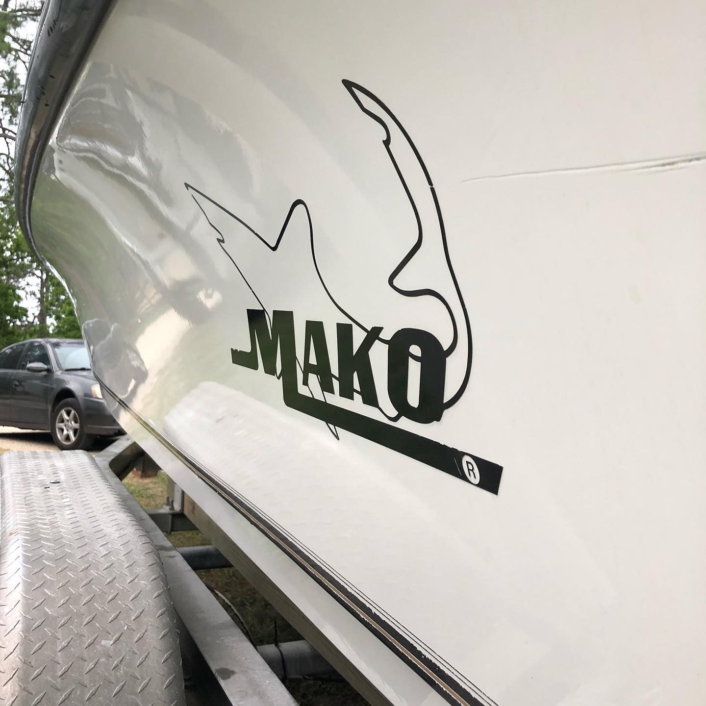 Close-up of a white boat hull with black MAKO logo decal and gray dock surface beside it