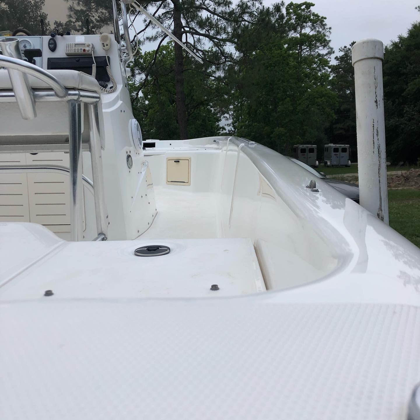 White boat deck with seating area and a dock post, near trees and water.