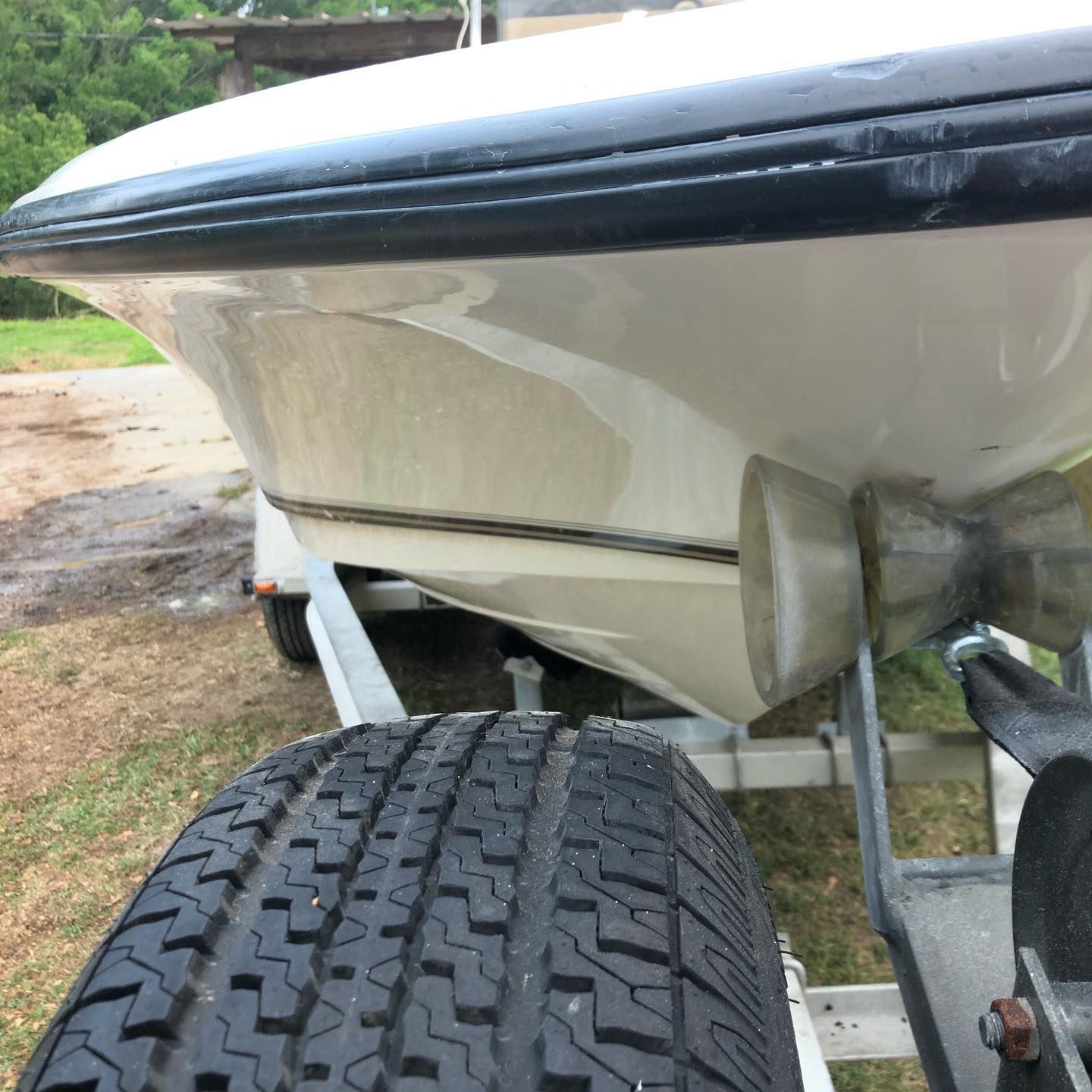 Close-up of a white boat on a trailer, showing the hull and treaded trailer tire.