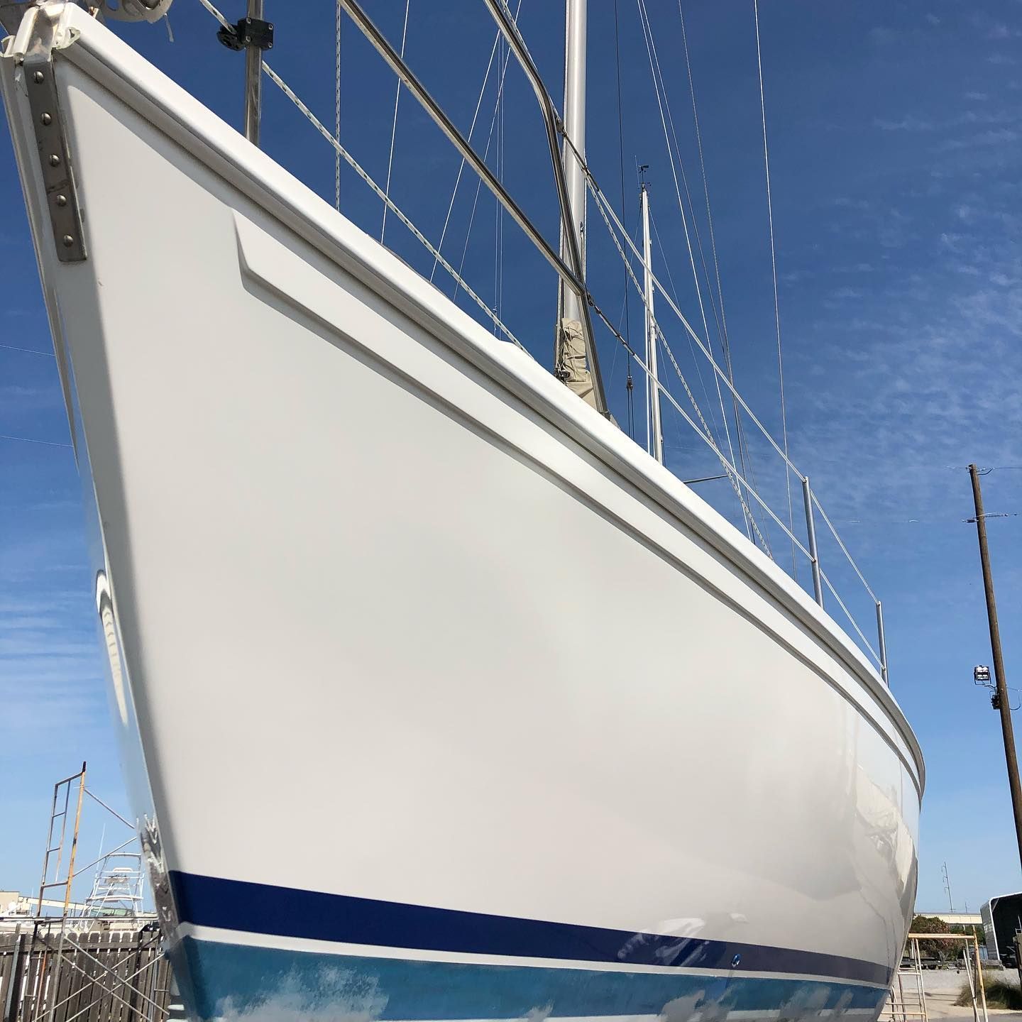 White sailboat hull with blue stripe, viewed from the side under a clear blue sky