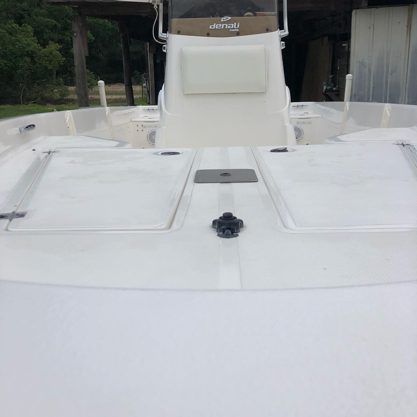 White boat deck with storage hatches and a center console under a canopy, viewed from the bow