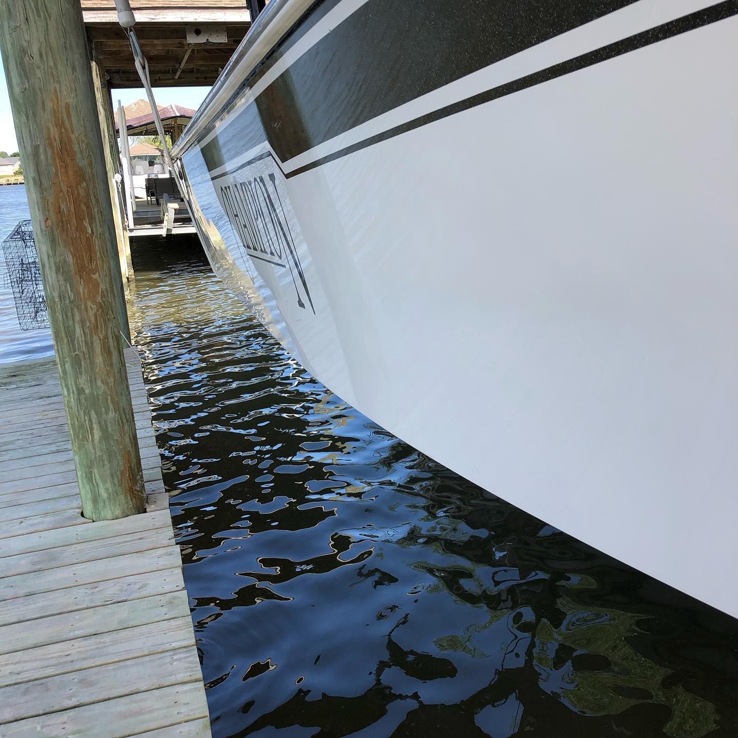 White boat moored beside a wooden dock, with water reflecting the hull and pilings.