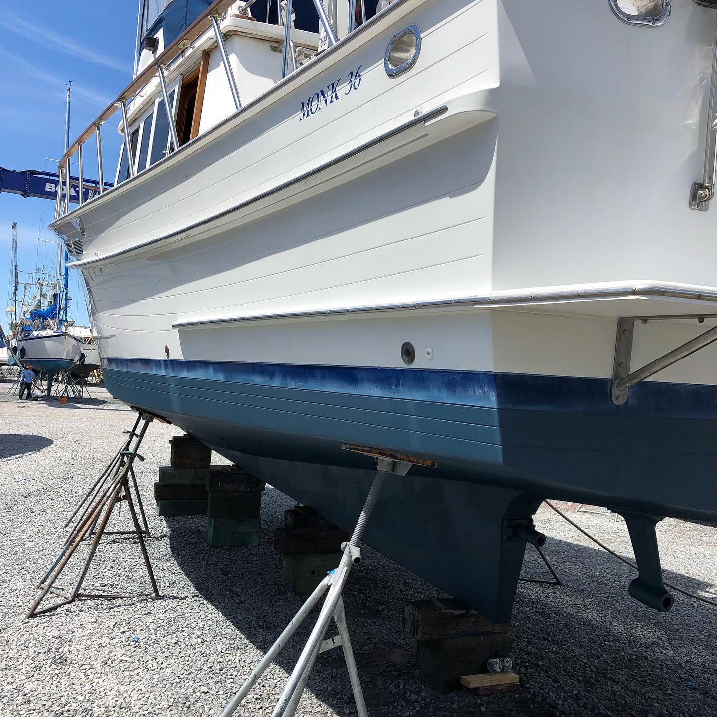 White boat on stands in a boatyard, with a blue hull and gravel ground.