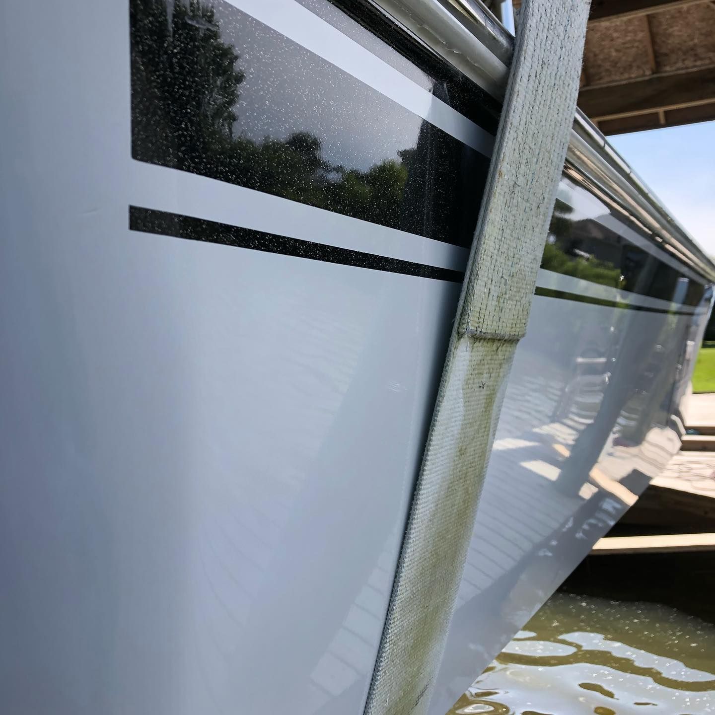 White boat hull with black stripes docked in shallow water, viewed close-up along the side