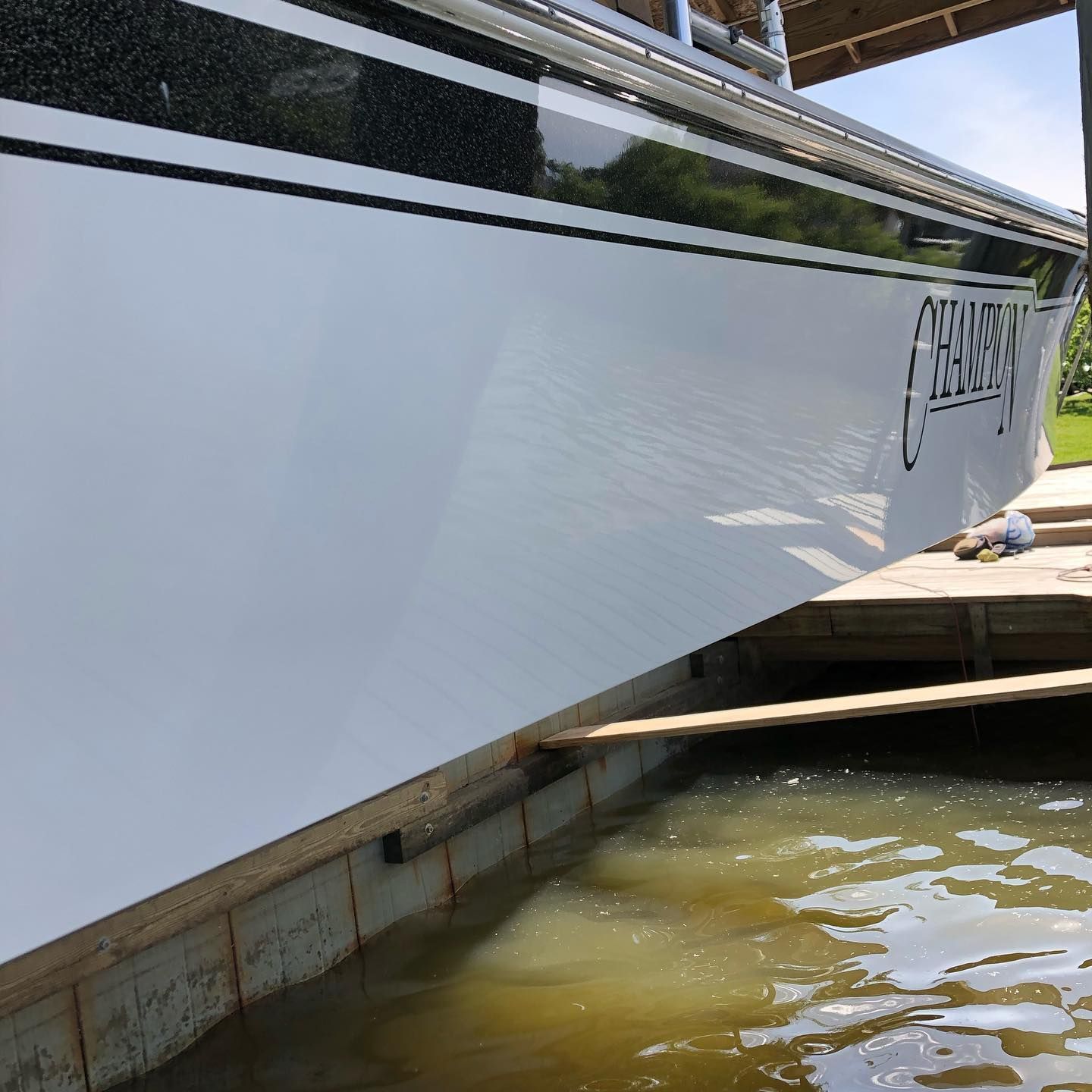 White boat hull in a docked boatyard, with water below and wooden supports underneath.