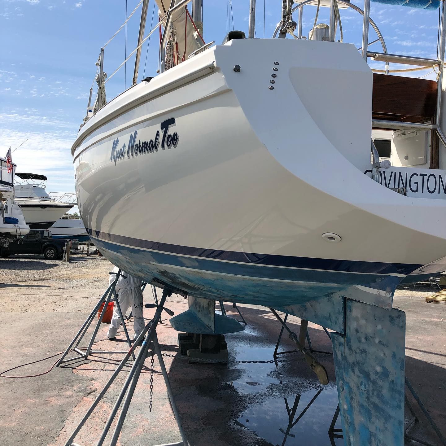 White sailboat on stands in a boatyard, with blue hull trim and a name on the stern.