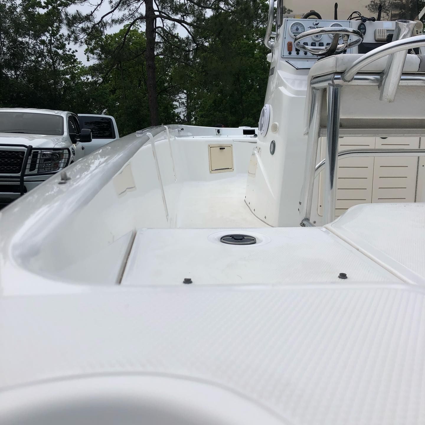 White boat deck with seating and railings, parked near trees and other vehicles.