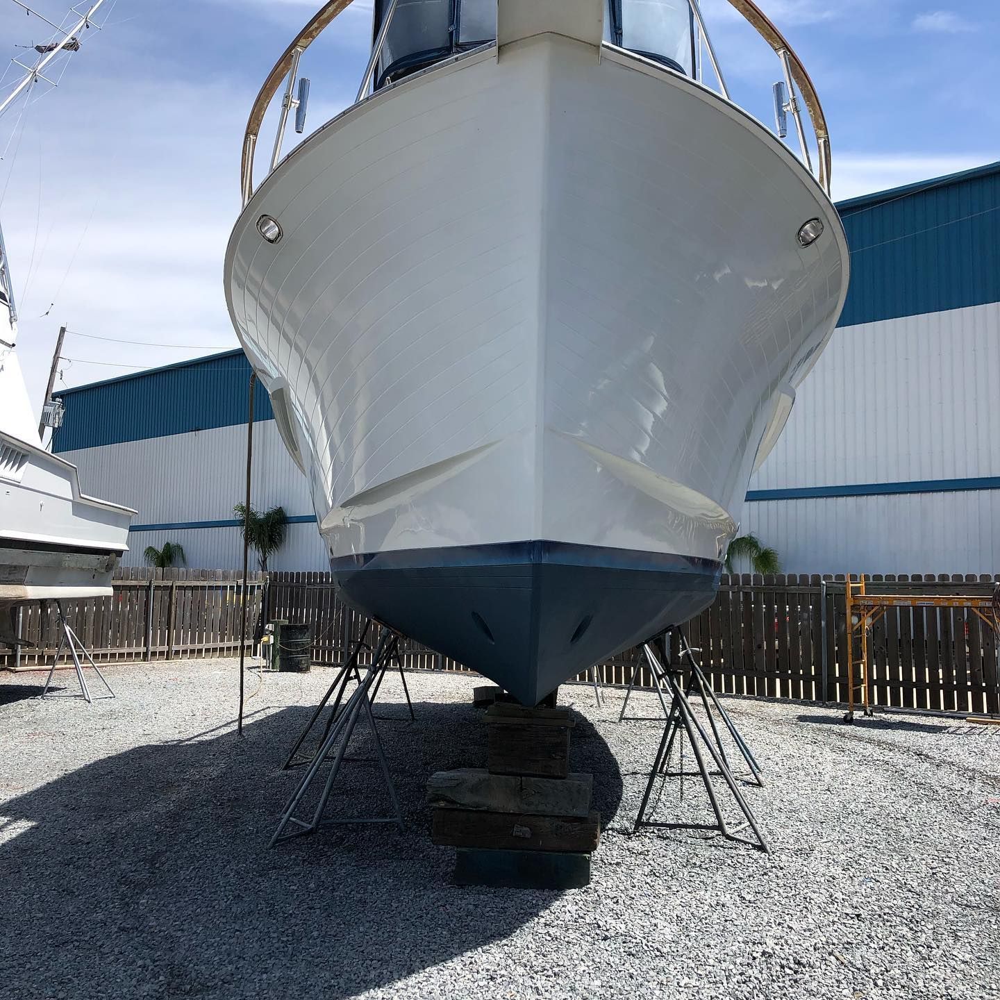 Large white boat hull on stands in a gravel yard beside an industrial building